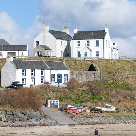A woman walks with her two dogs near white houses by the shore at the southwest tip of Islay, Scotland