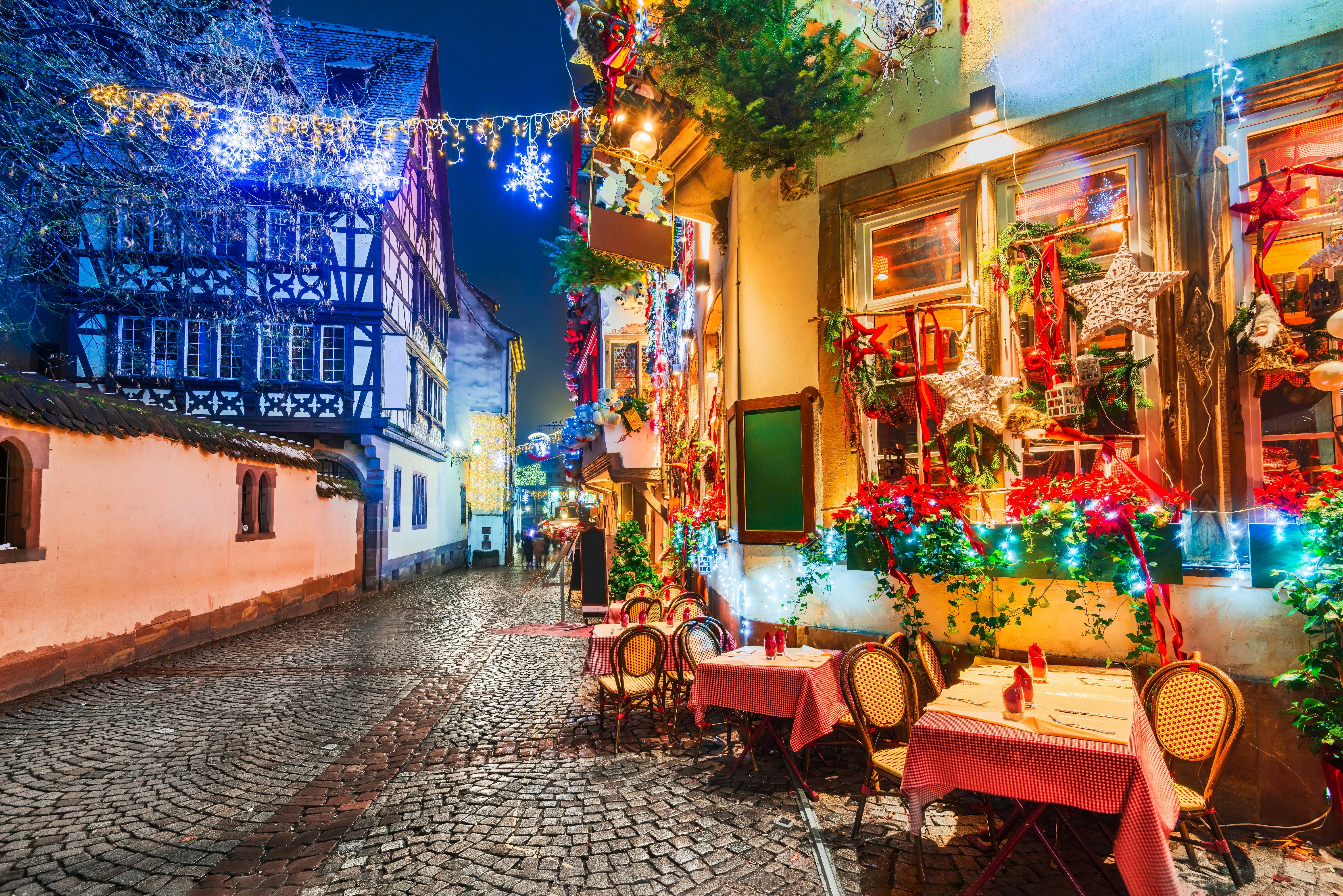 A cobbled street and restaurant with Christmas lights and decorations on a winter's evening.