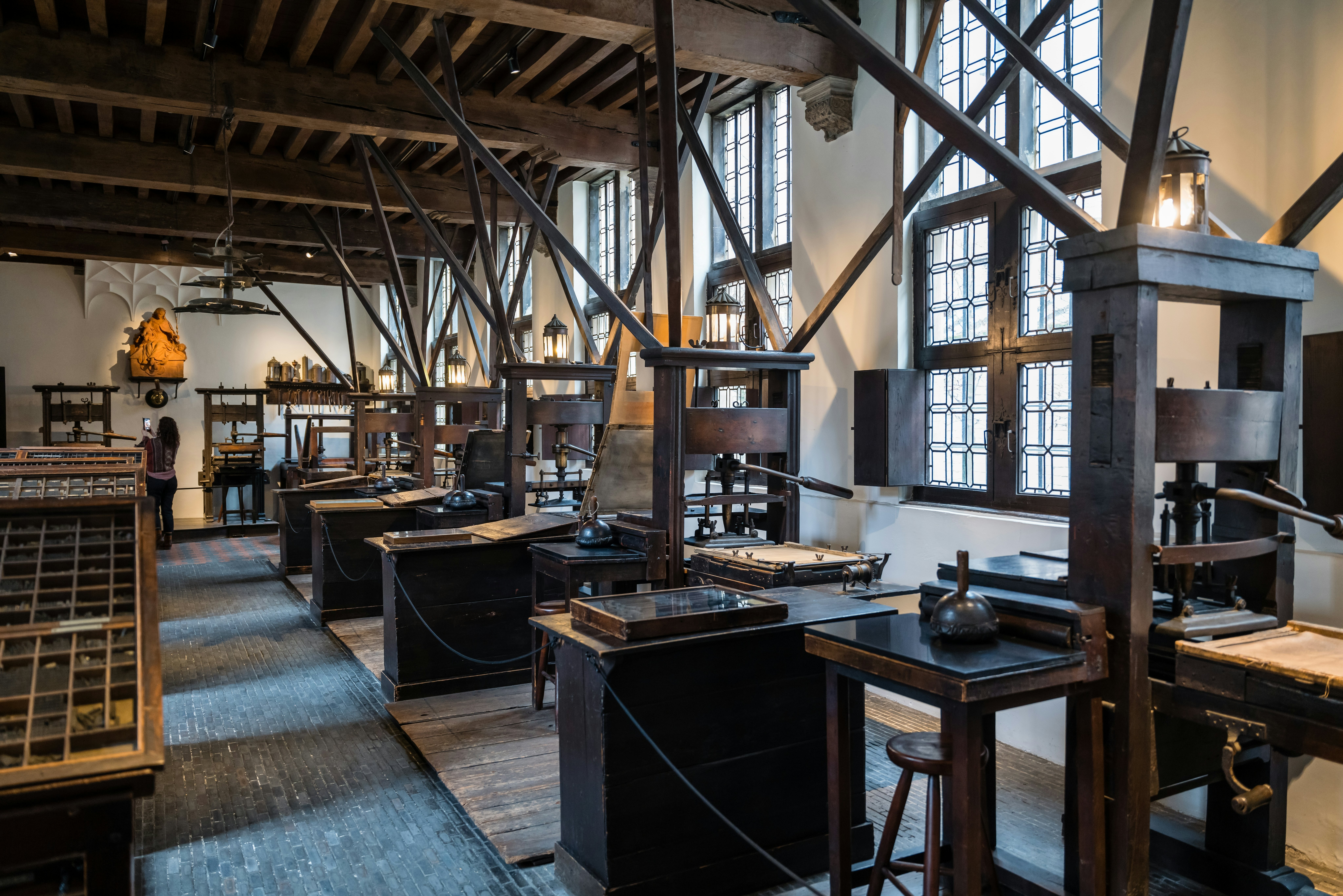A row of antique printing presses is on display at a museum that occupies a historic house in a city.