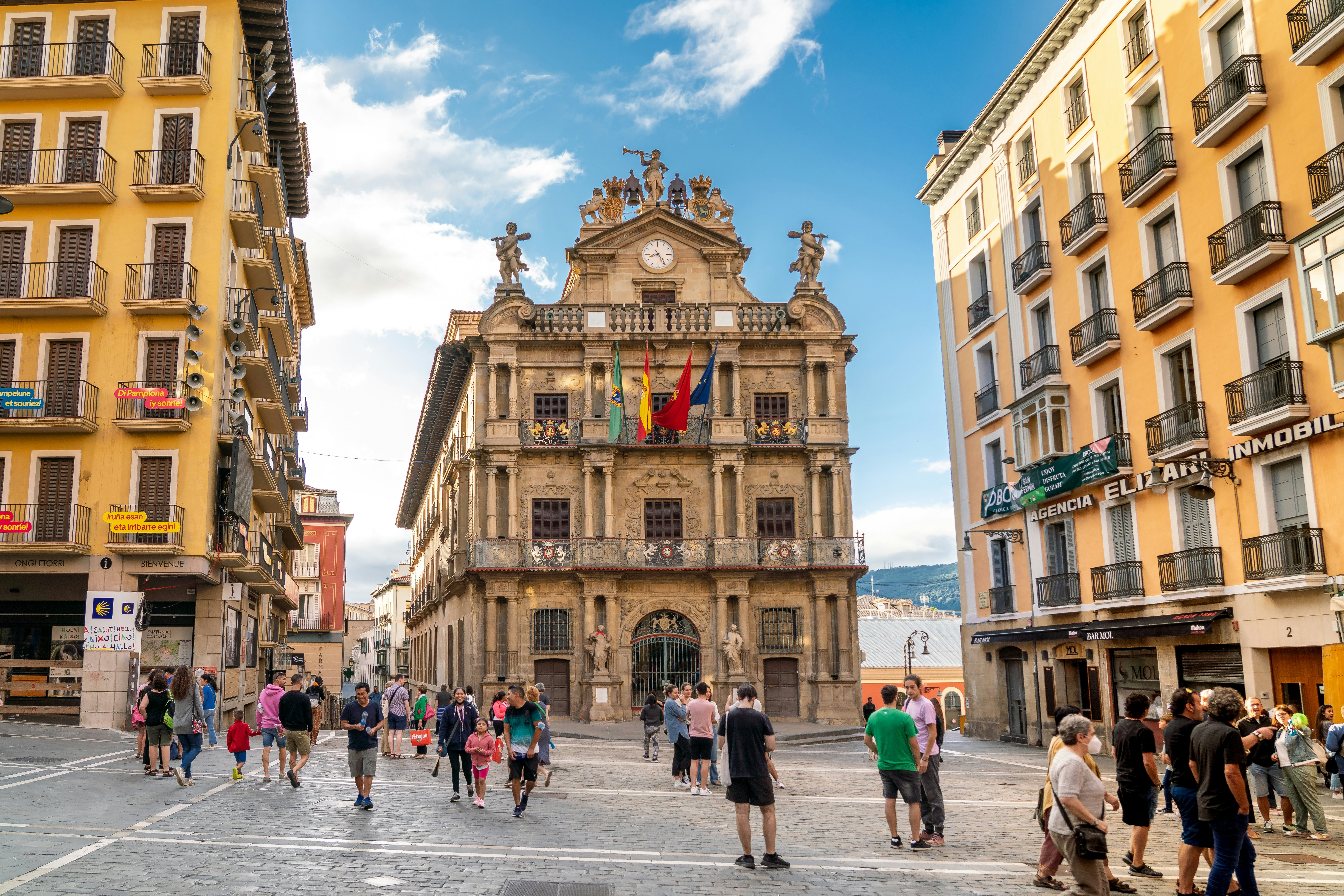 People wander through a city square lined with buildings.