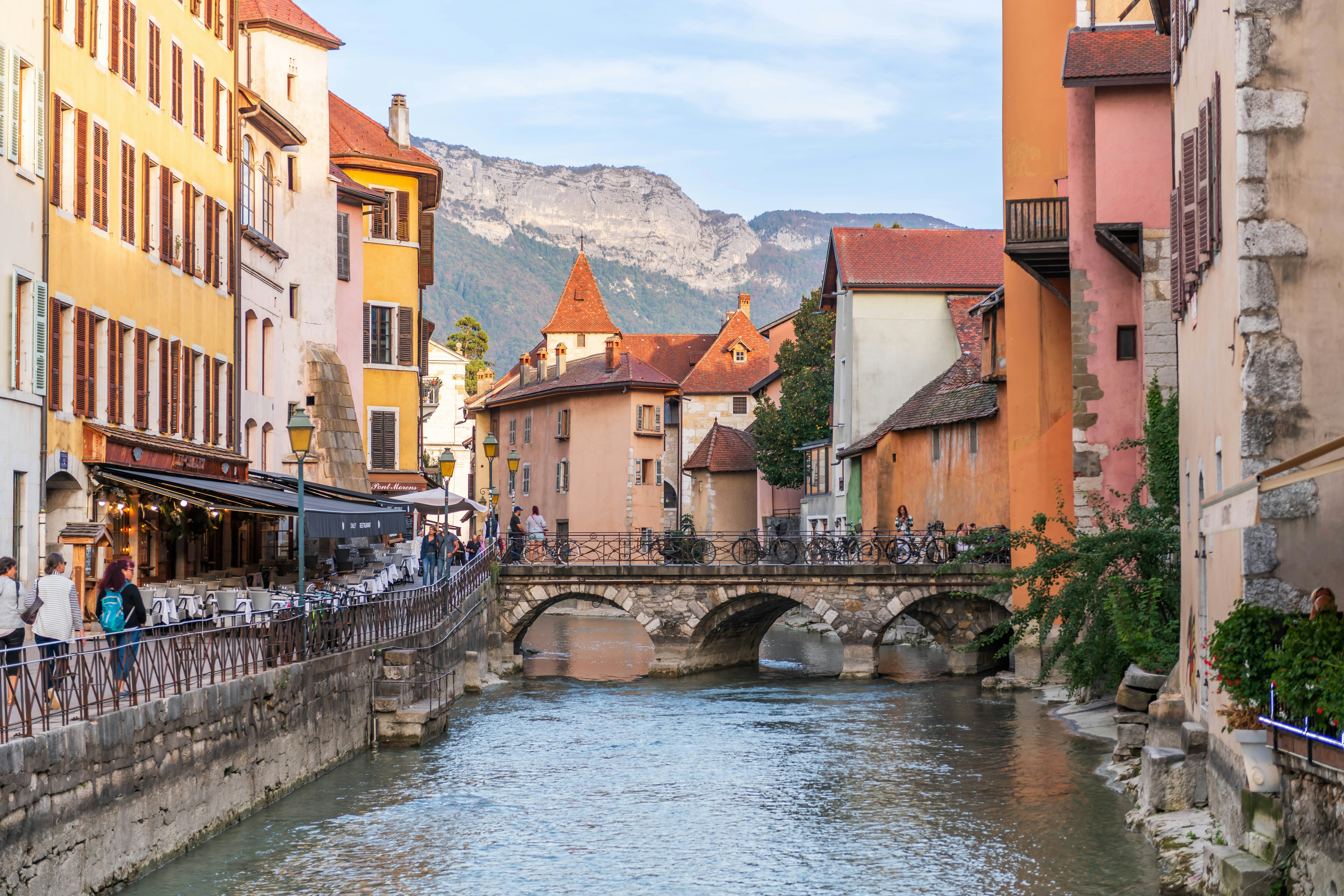 A river lined with pastel-colored buildings backed by mountains.