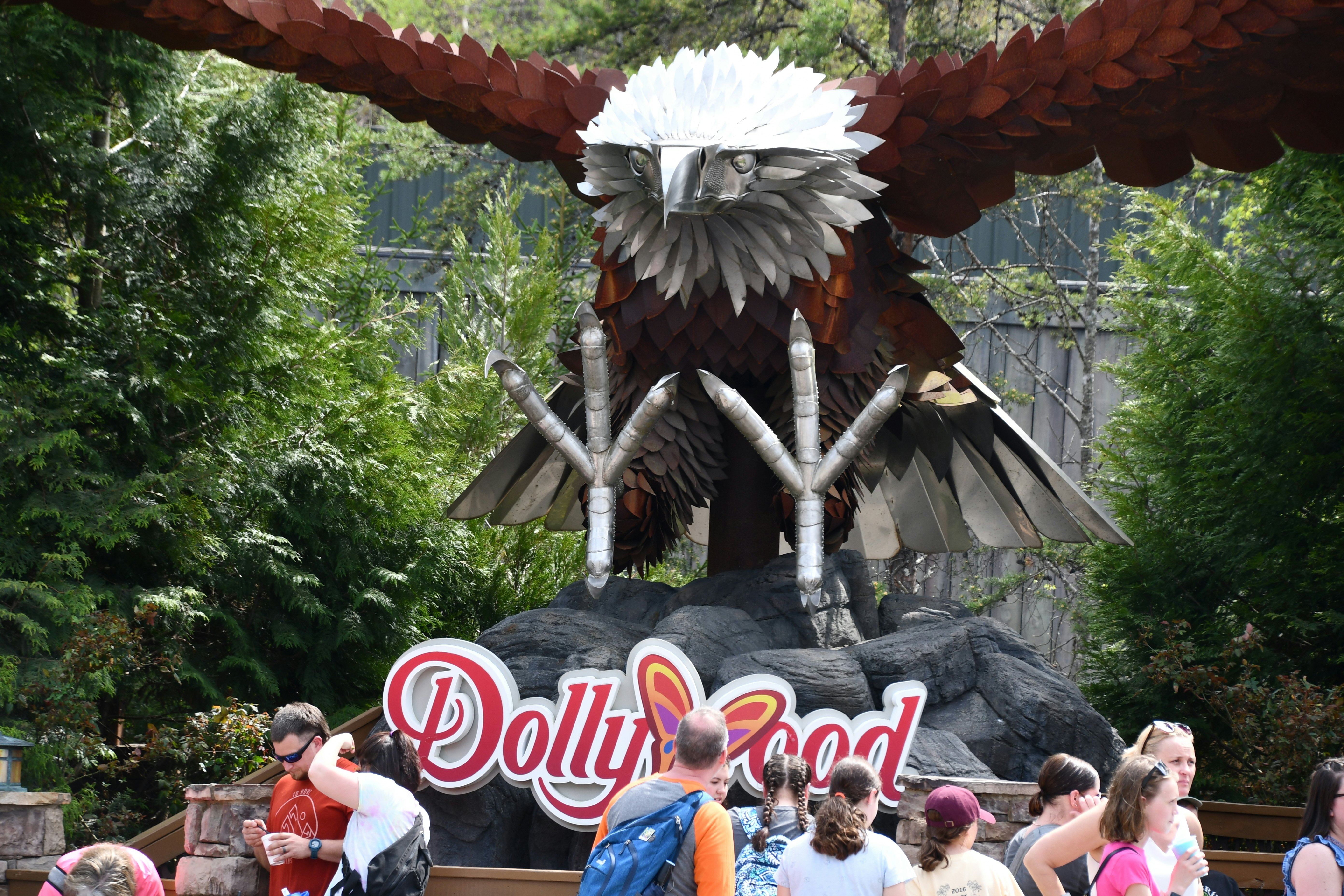 People at an amusement park stand in front of a giant wooden sculpture of a bald eagle.