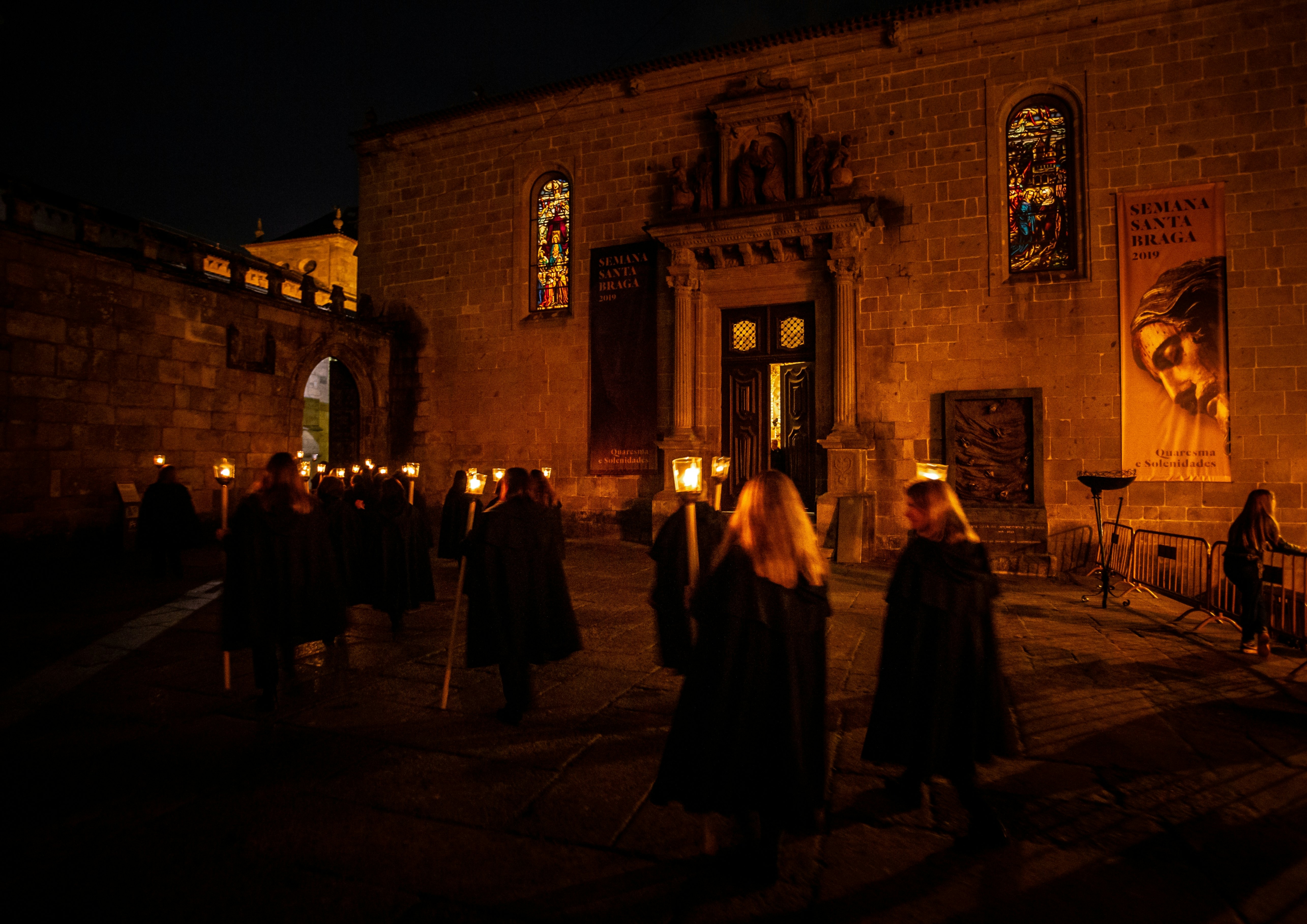 People in hooded robes carry torches down a city street during a nighttime religious procession in Portugal.