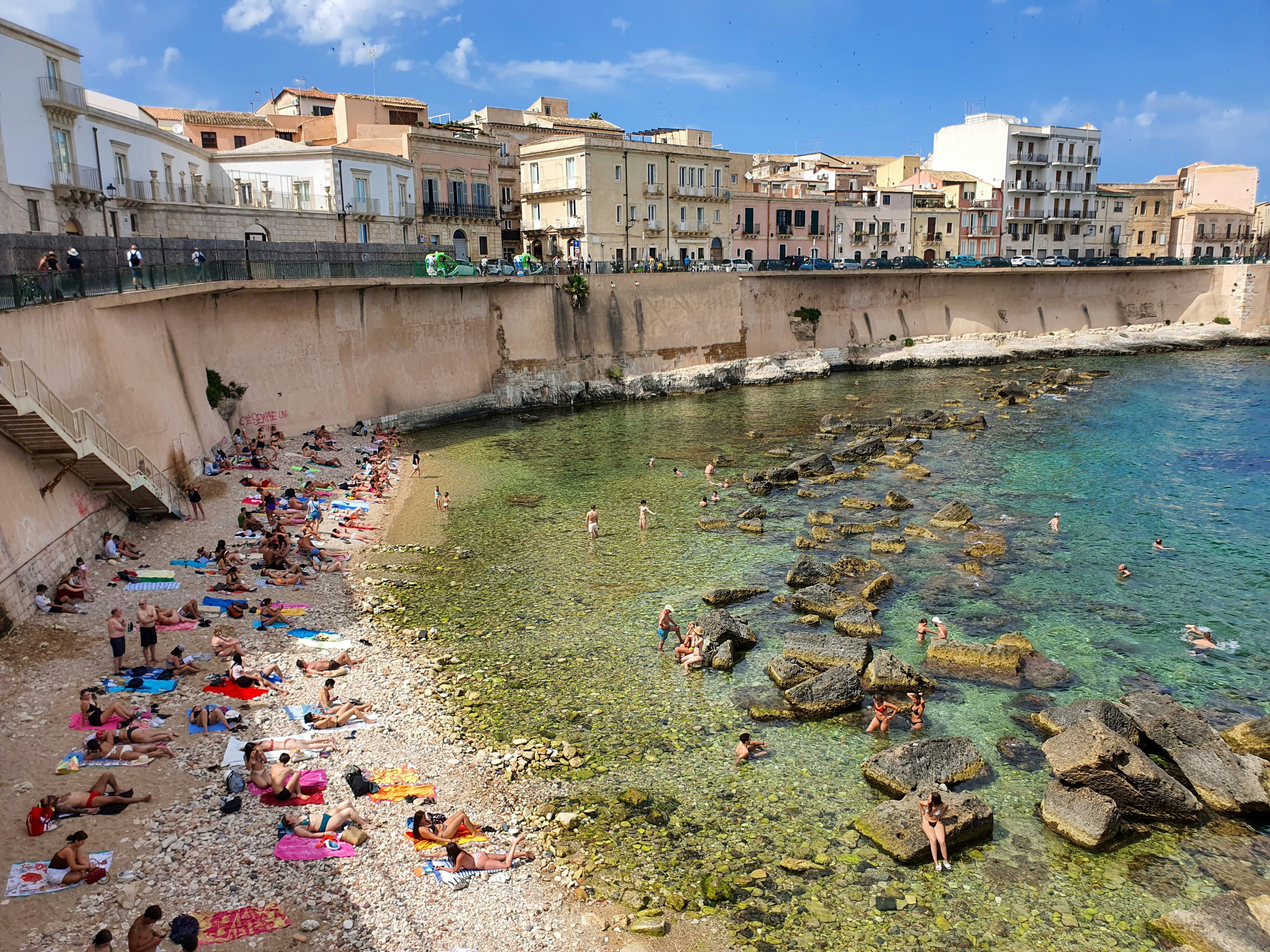 People relax on a rocky beach at Ortygia in Syracuse, Italy.