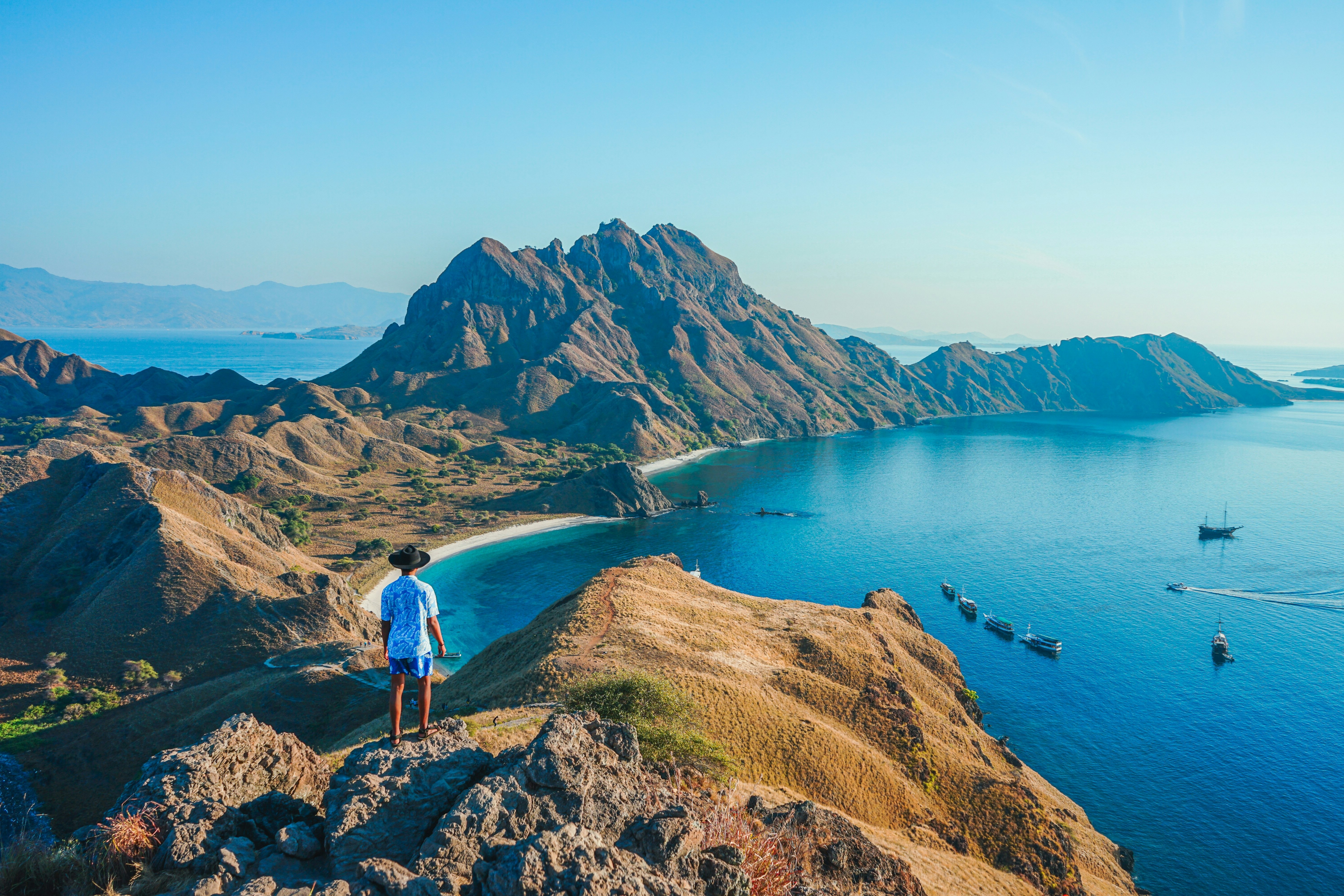 A man stands at a viewpoint looking down at the coastline of a mountainous island.