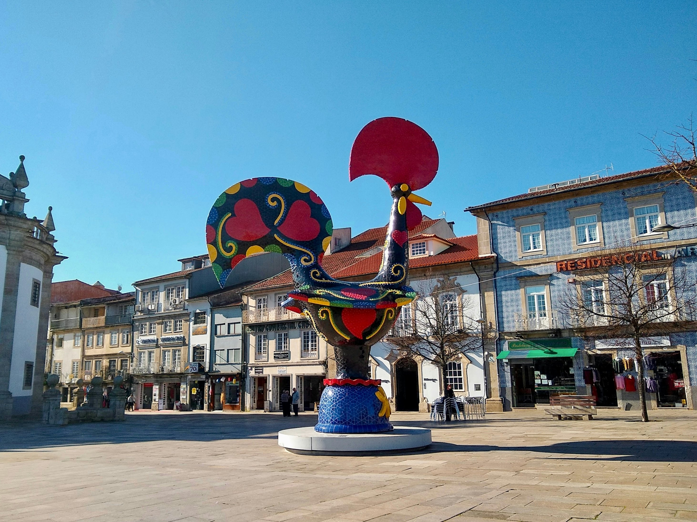 A brightly painted sculpture of a rooster sits in a town square in Portugal.