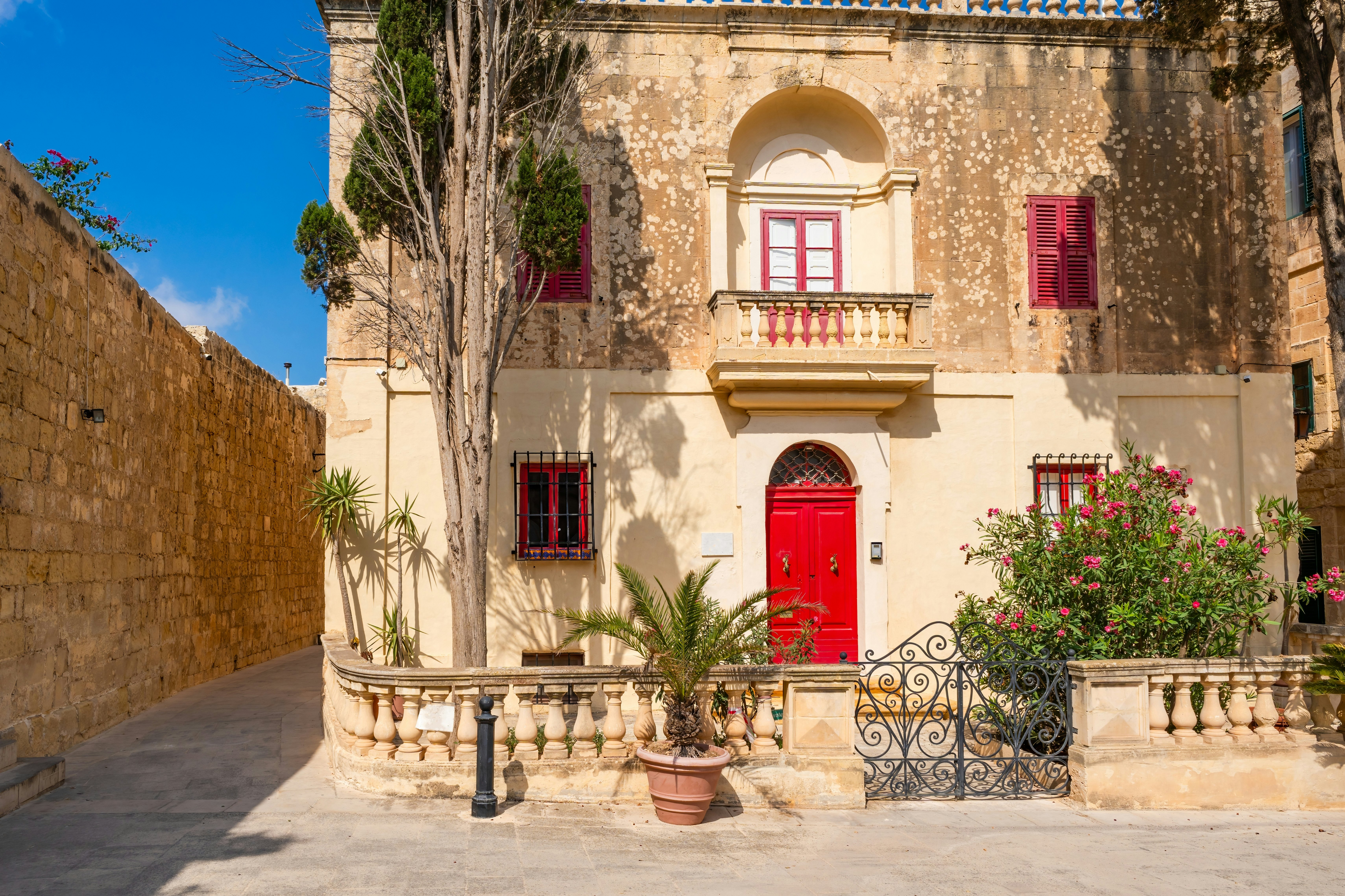 A two story honey-colored home with windows framed by red shutters and a red door.