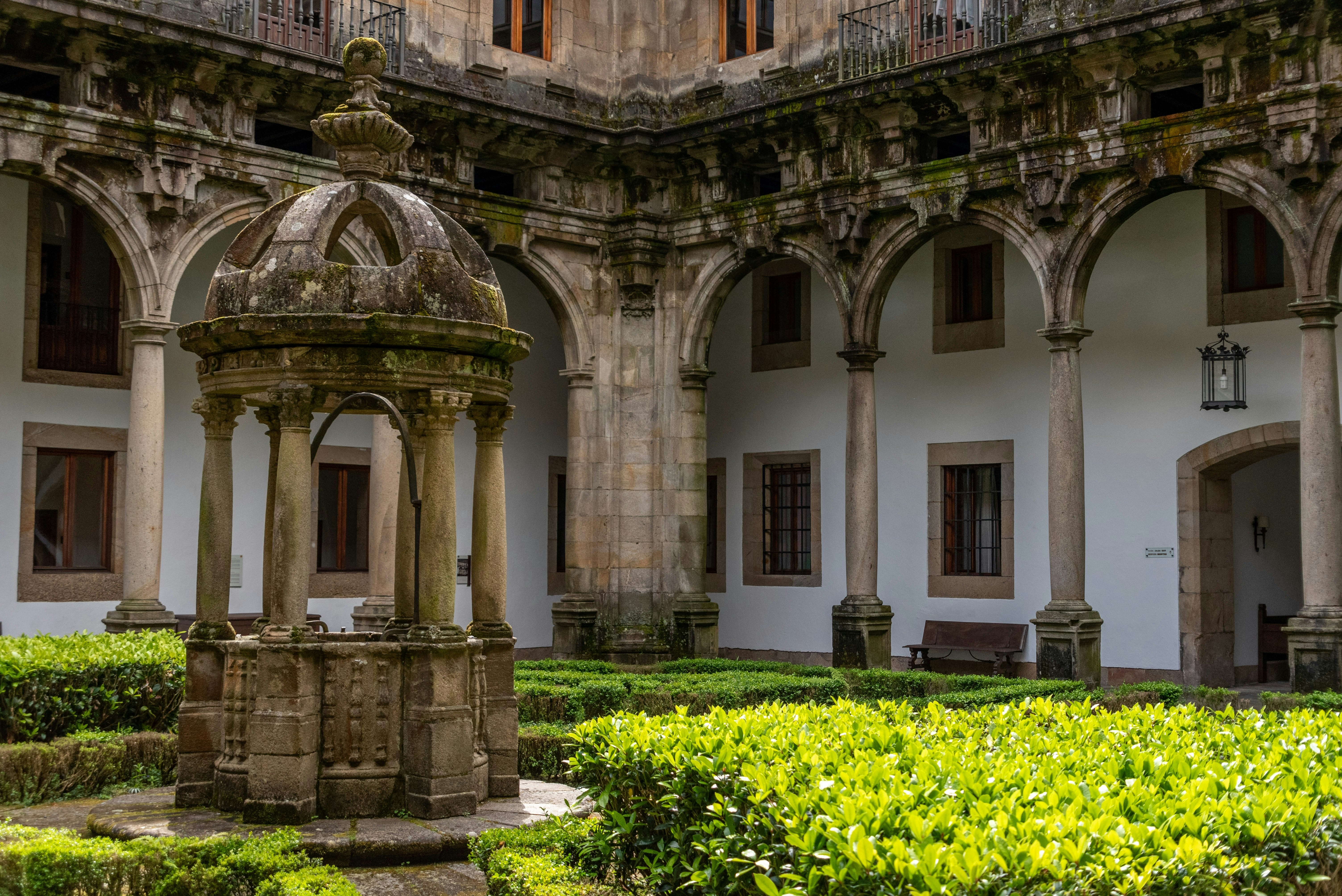 A courtyard with greenery and stone gazebo with an old white-and-stone building in the background.