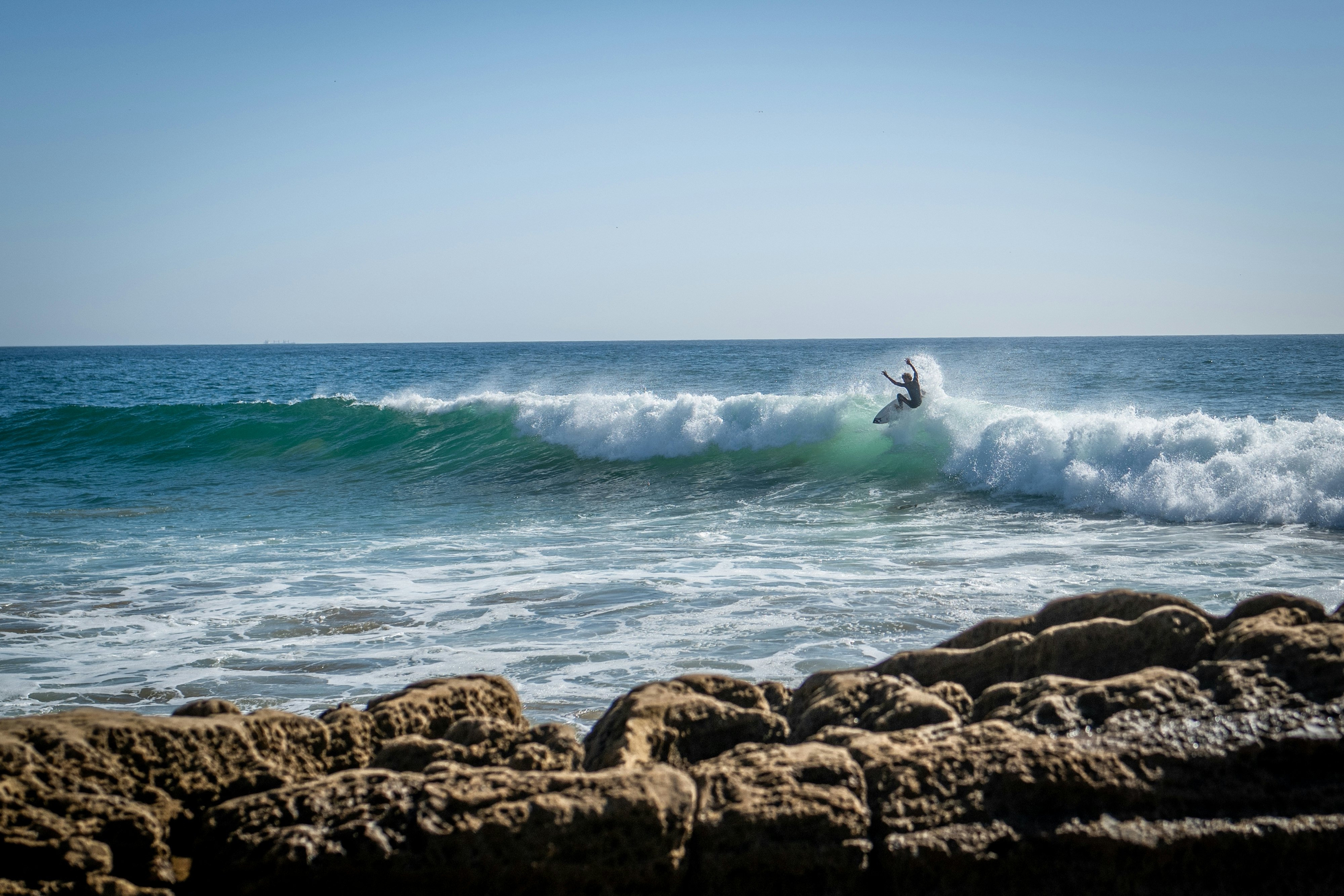 A surfer catches a wave adjacent to the shore.