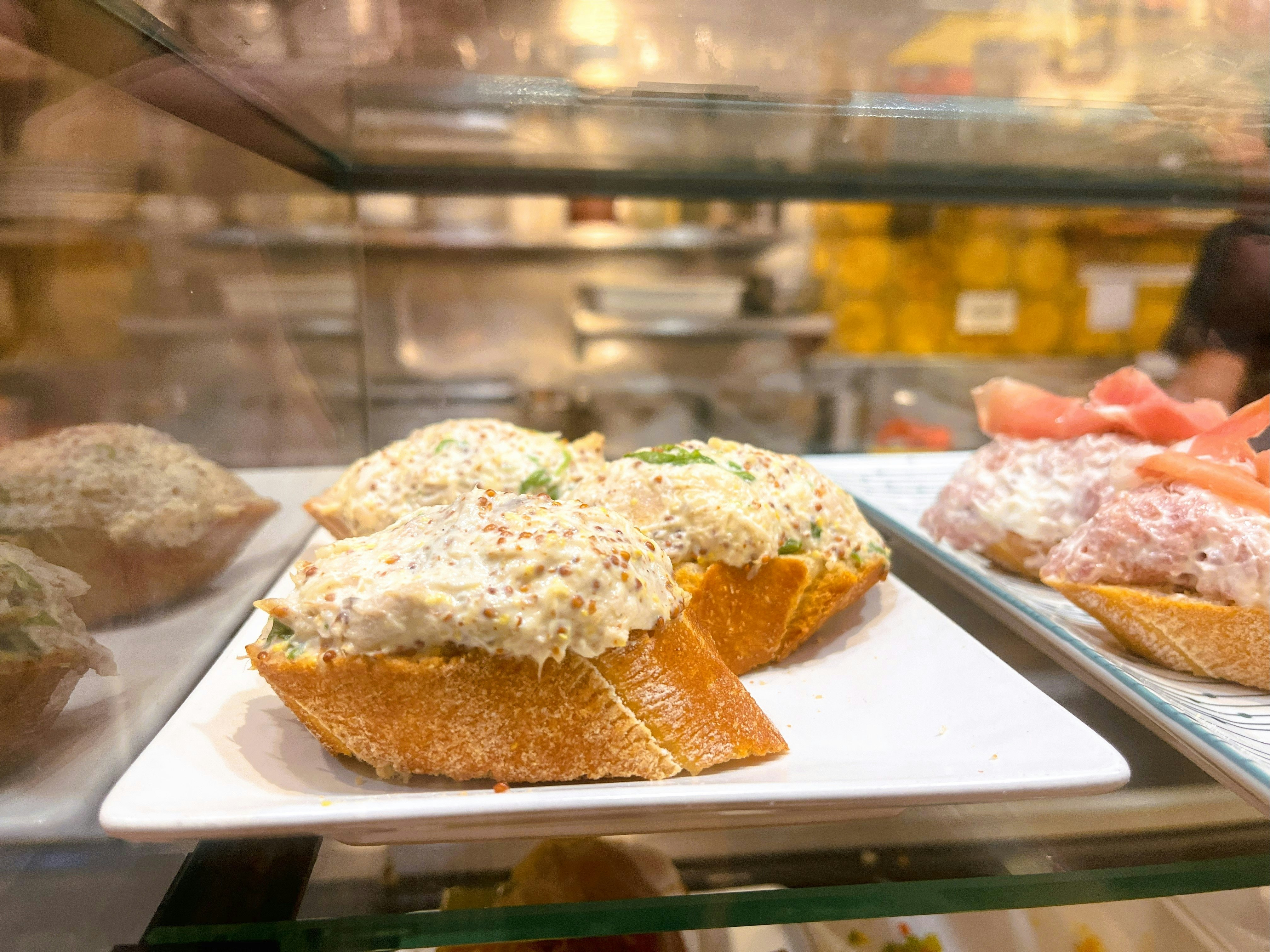 A slice of baguette with a paste on top on display at a counter in a bar.