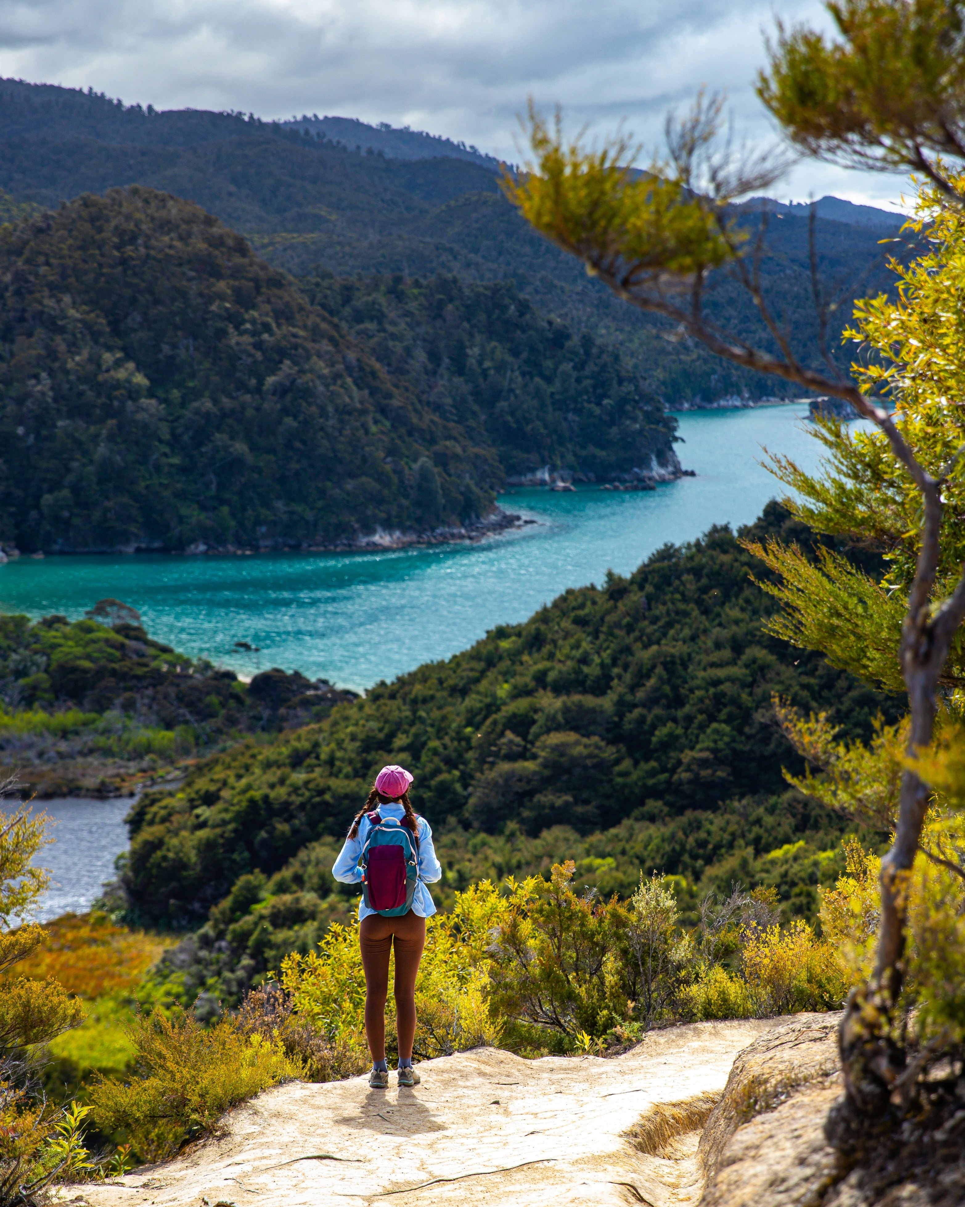 backpacker stands on the hill overlooking Anchorage Bay and Torrent Bay in Abel Tasman National Park - hiking on a famous great walk in New Zealand South Island