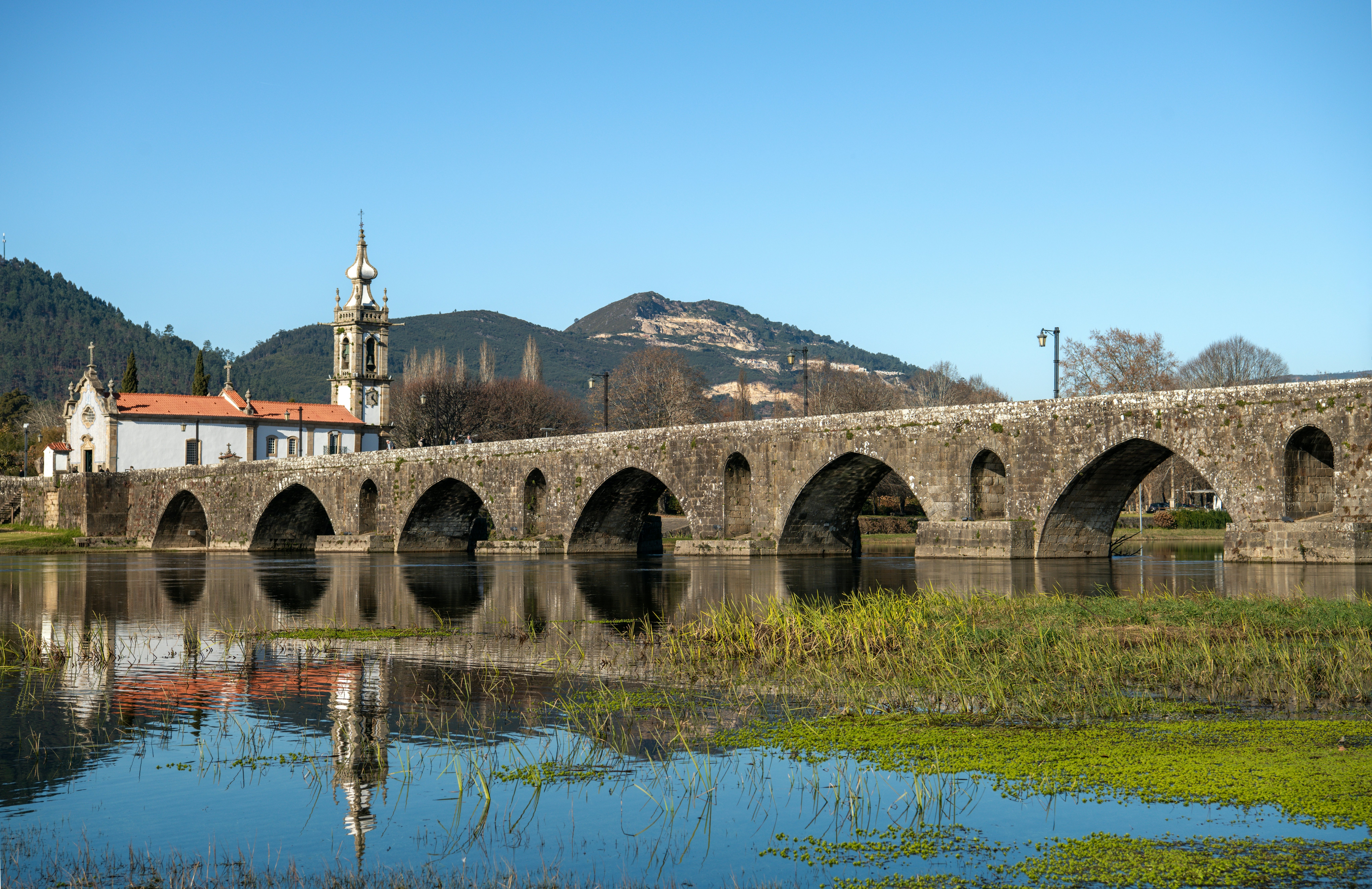 A masonry bridge with several arches spans a river. A church stands on one side of the bridge.