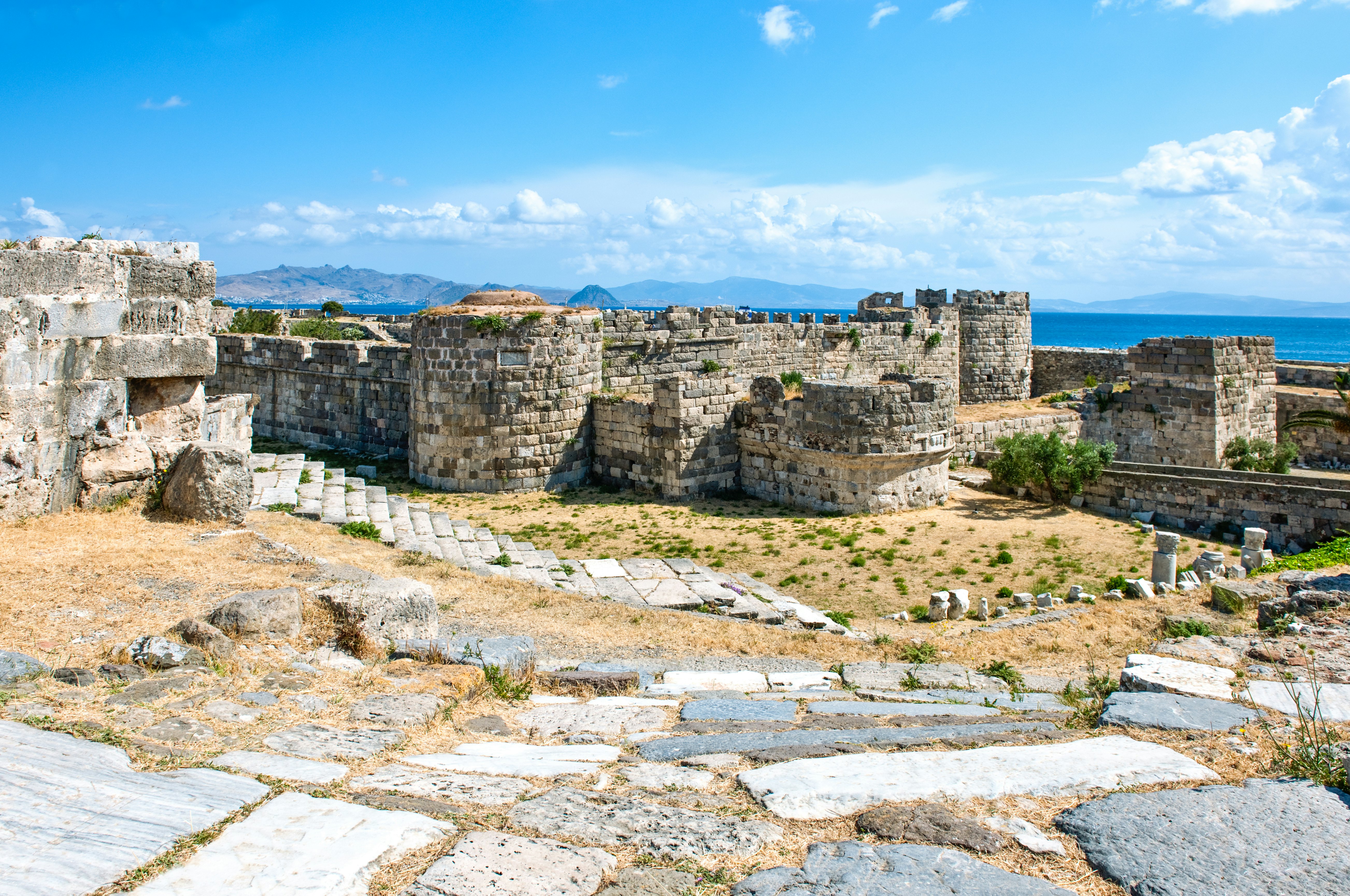 The exterior of a medieval castle is pictured, with the blue sea beyond.