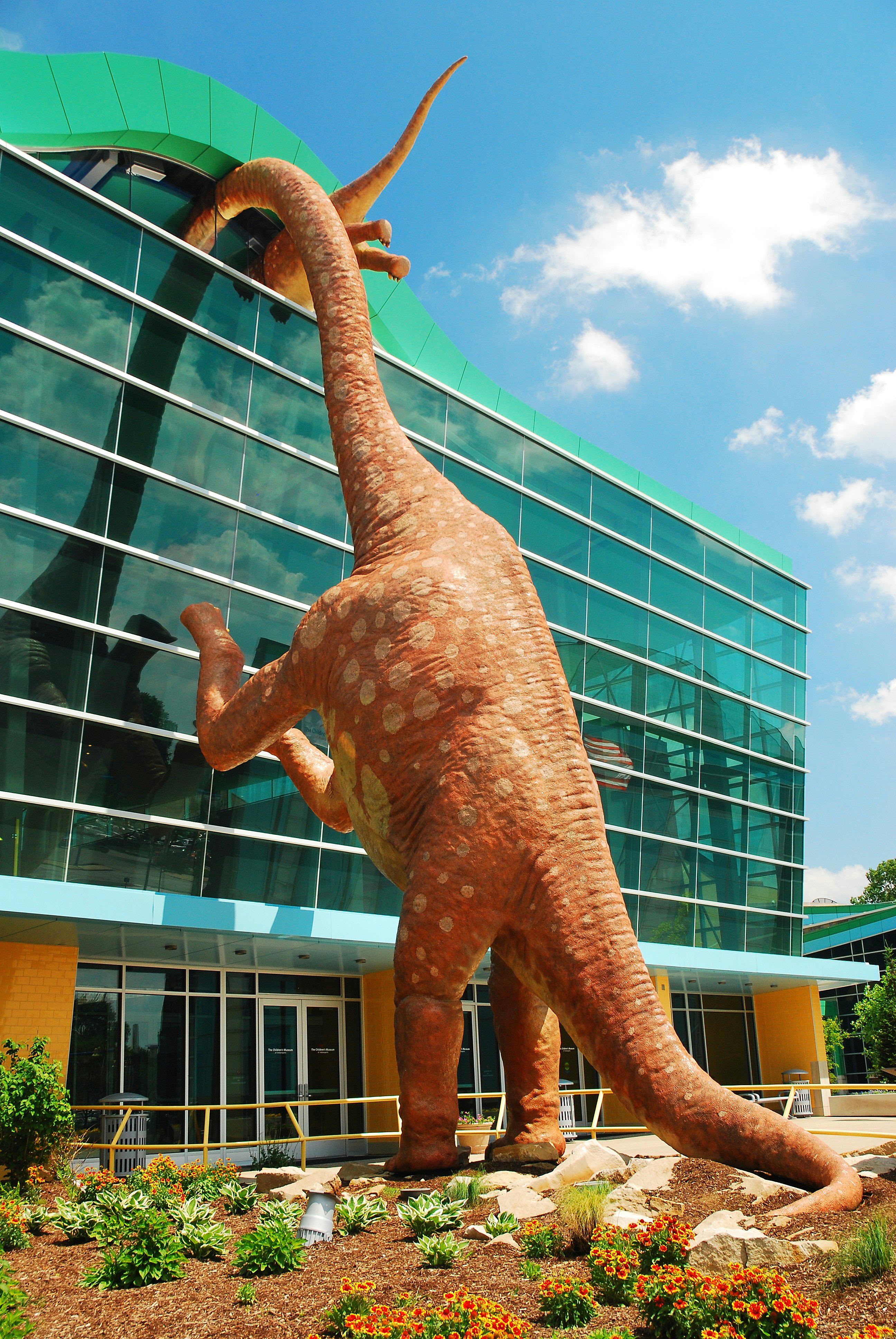 Statue of a dinosaur peeks into the windows of a glass building