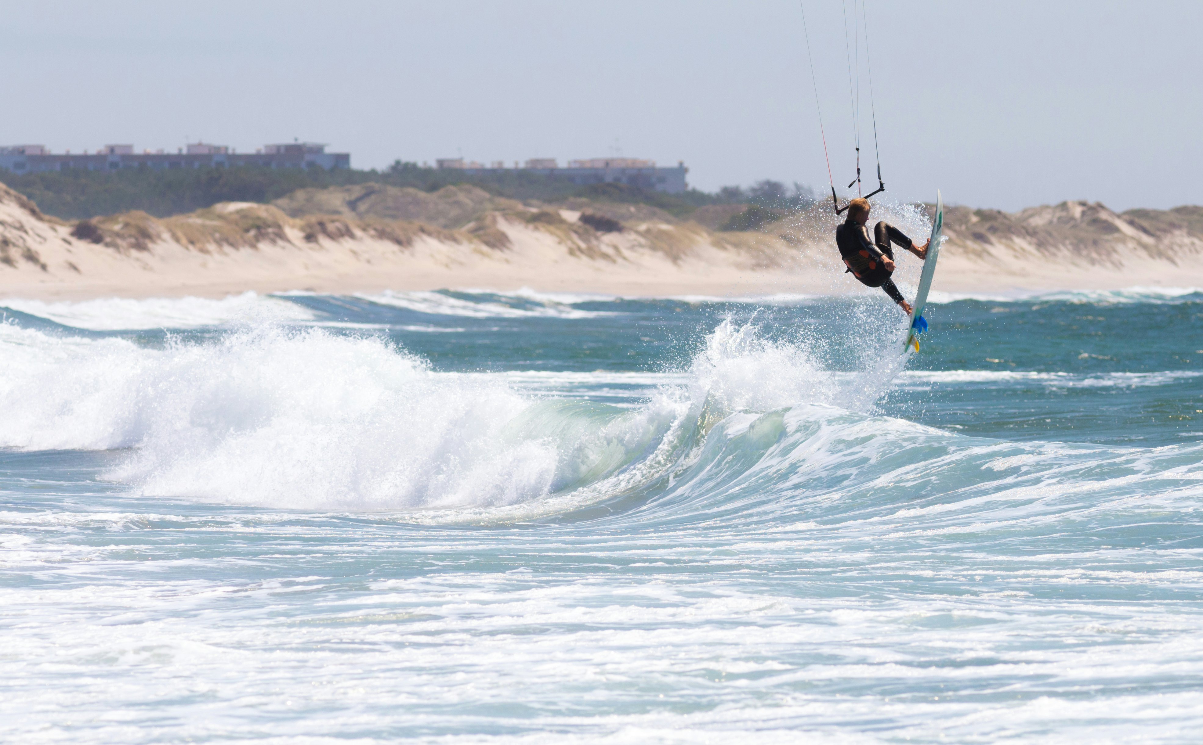 A kitesurfer flies into the air after riding a wave near a beach.