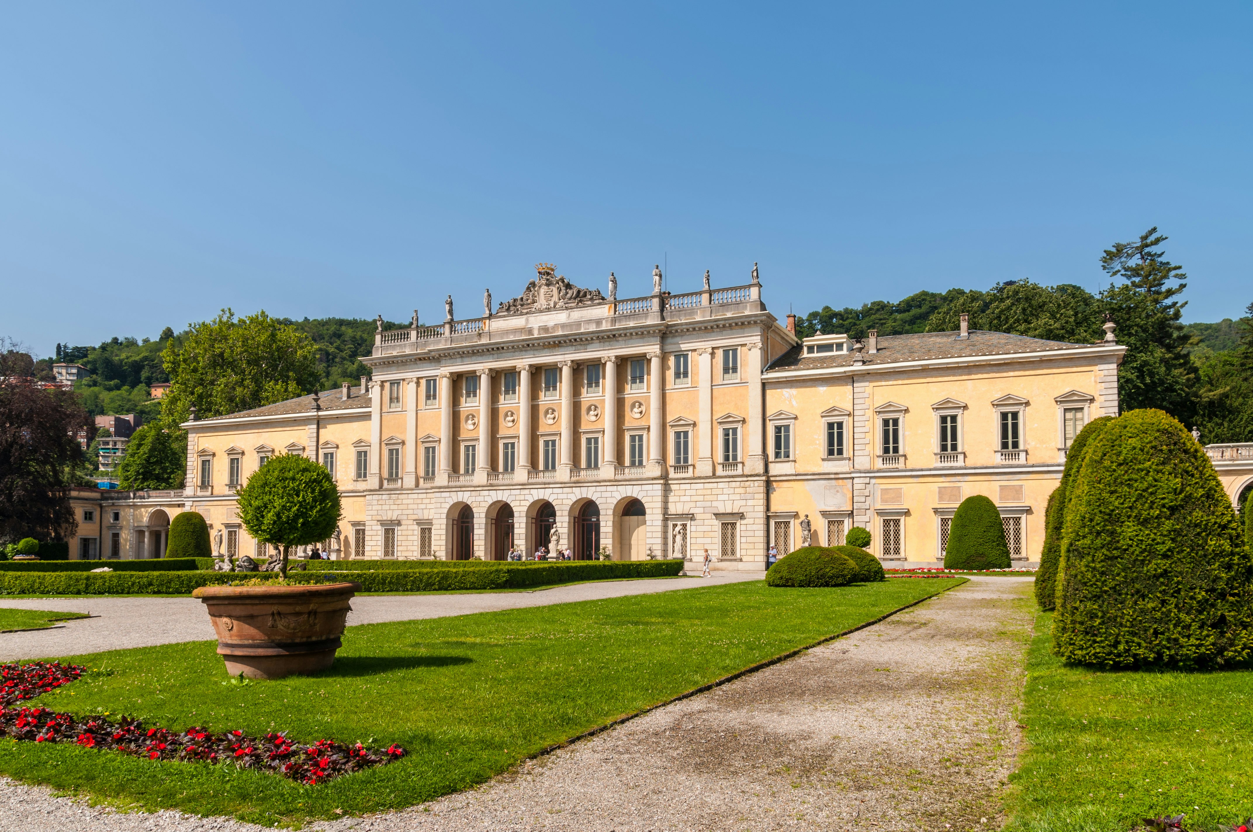 View of Villa Olmo on the lakefront in Como on Lake Como, with flowers and hedges in the foreground.