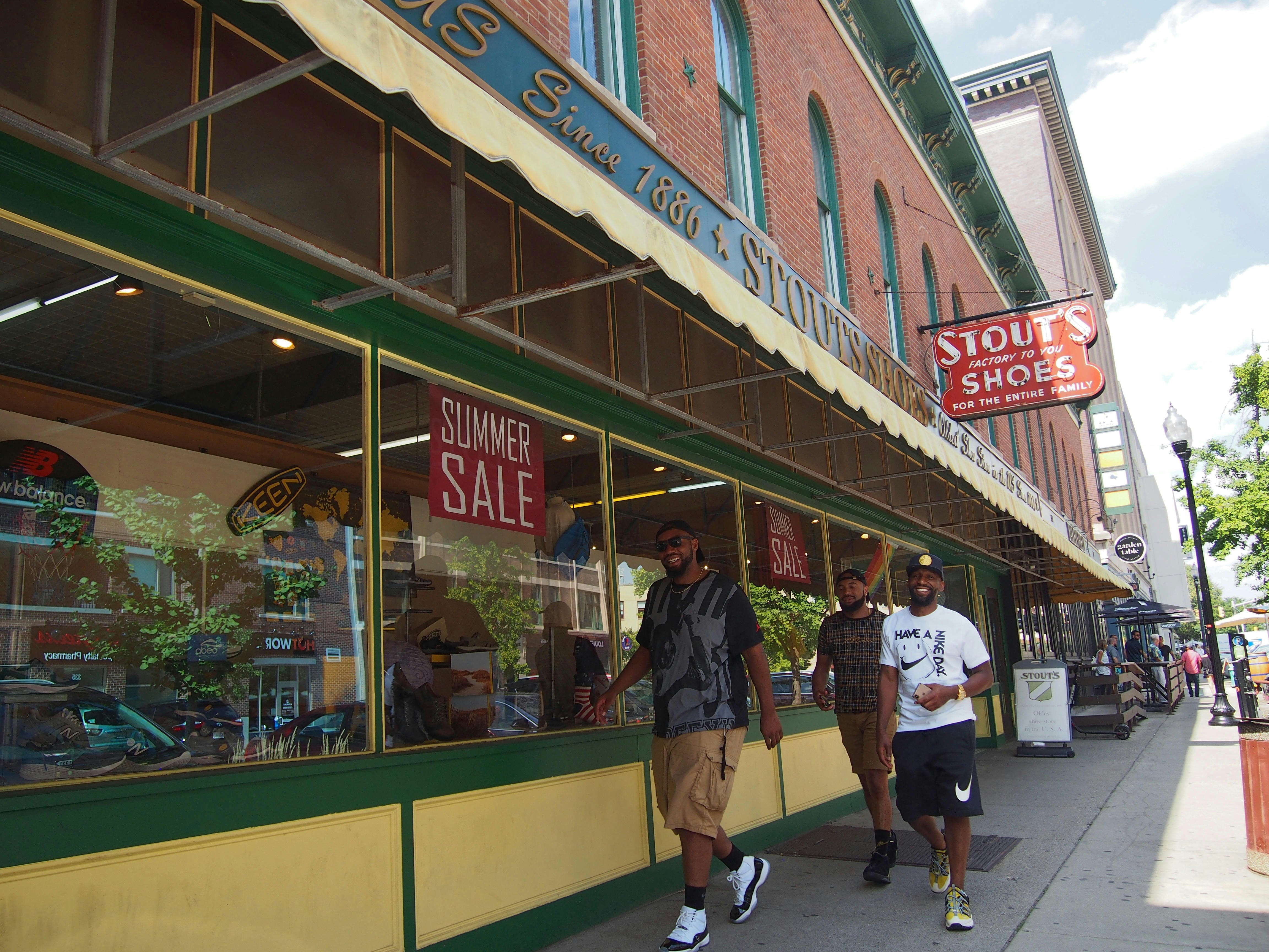 Three men walking by a shoe store that is advertising its summer sale with signs in the windows