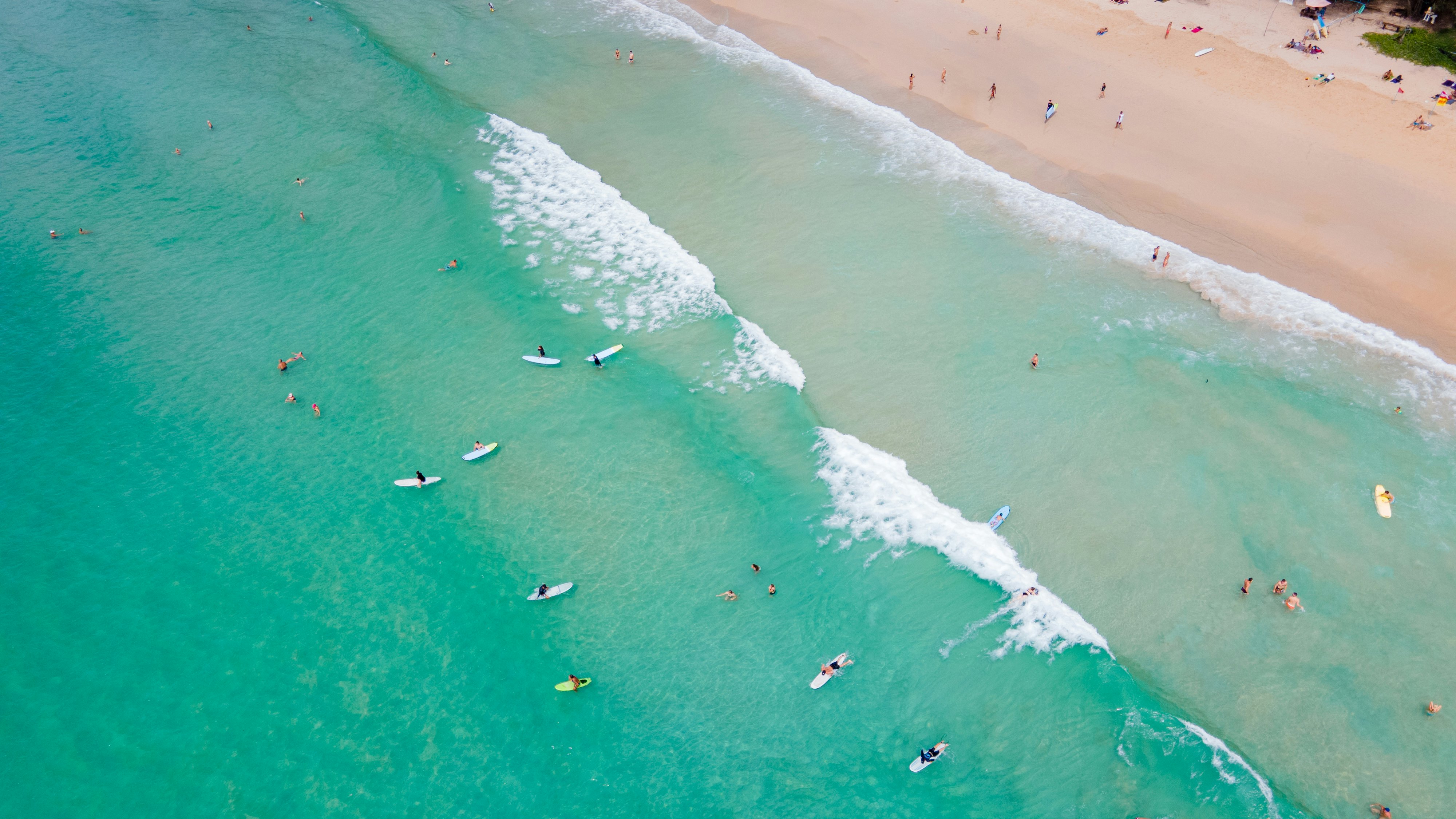 View of surfers riding waves from above as waves lap the shore