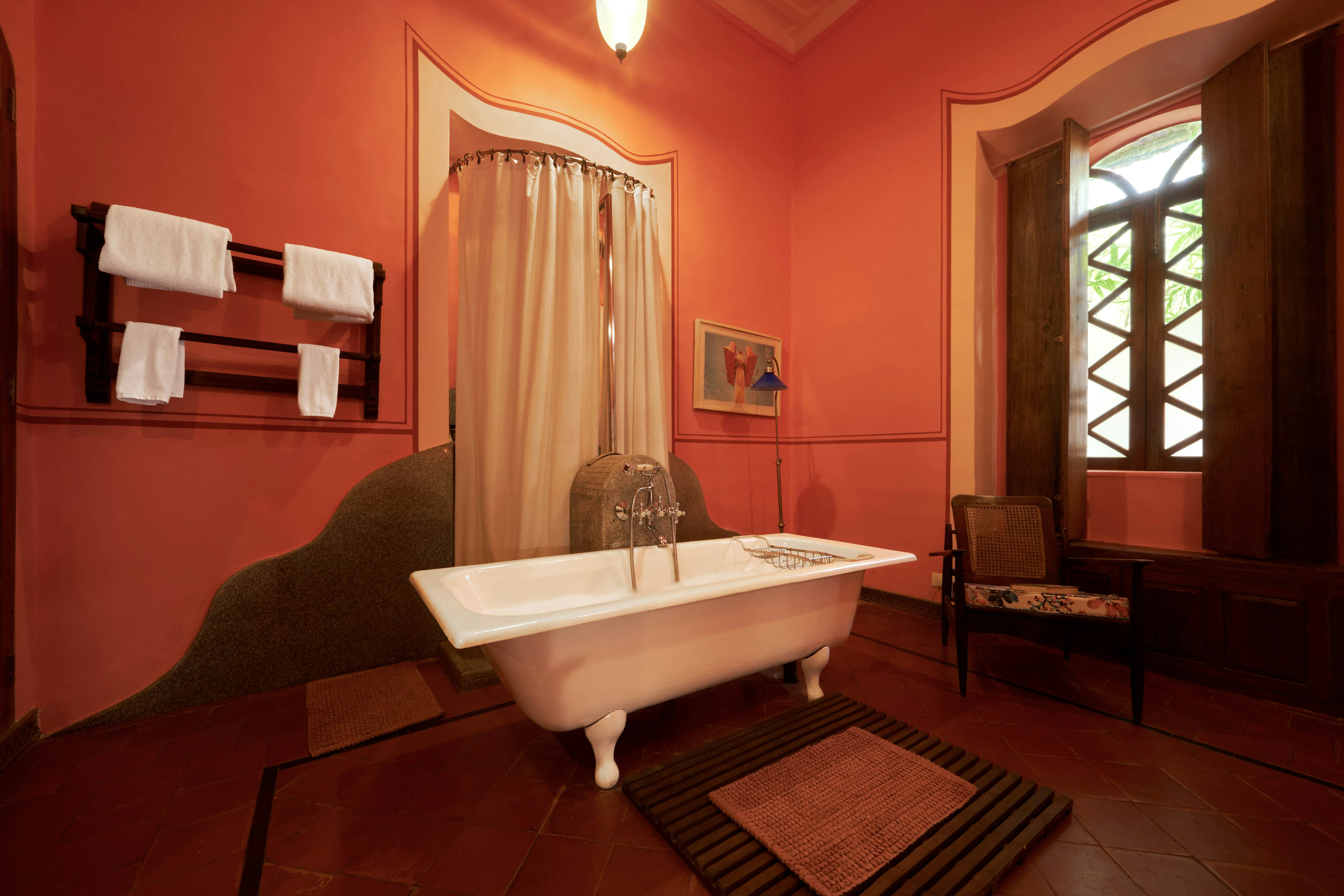 A freestanding bathtub in a hotel bathroom with red walls.
