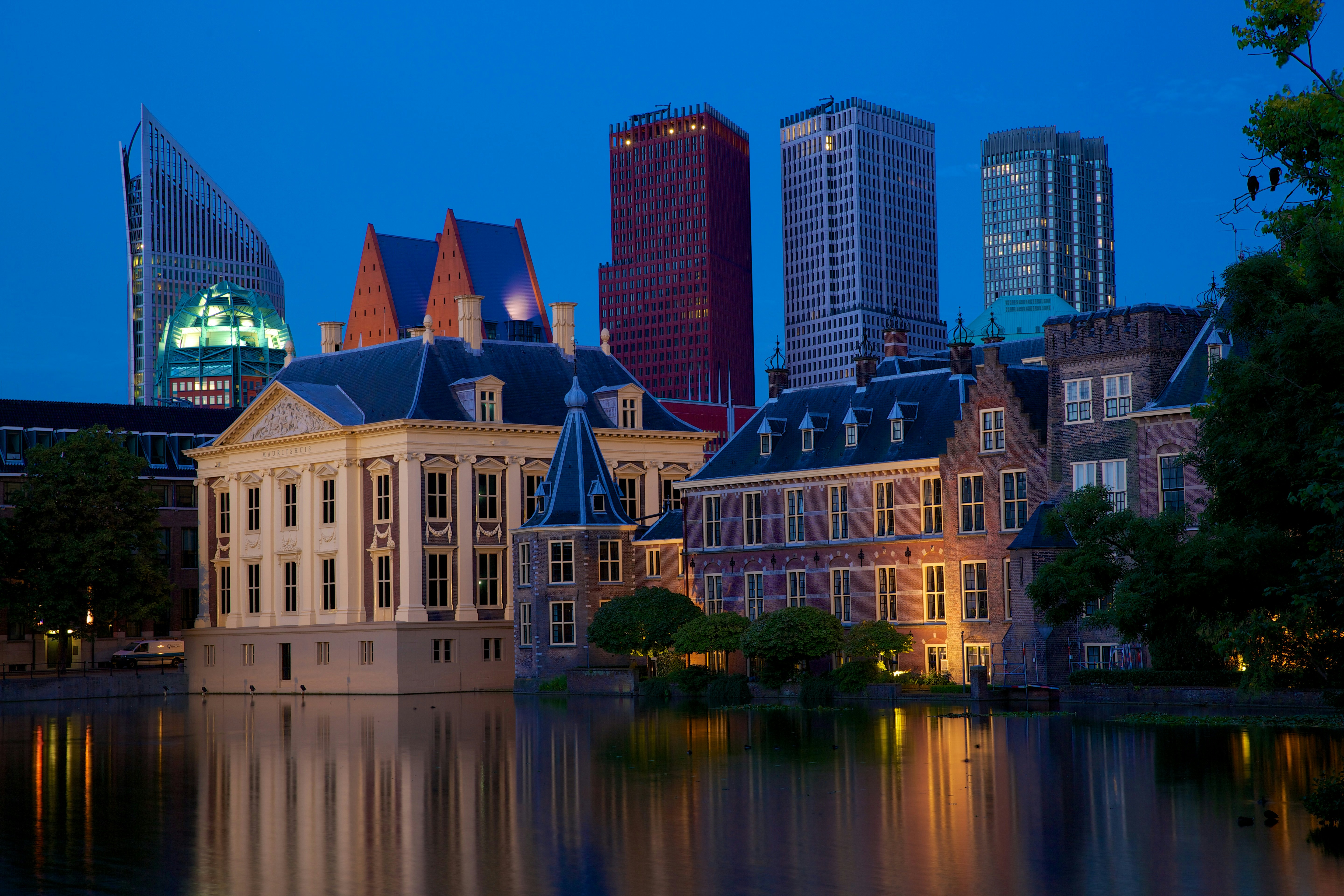 The Peace Palace at dusk with modern city buildings behind it