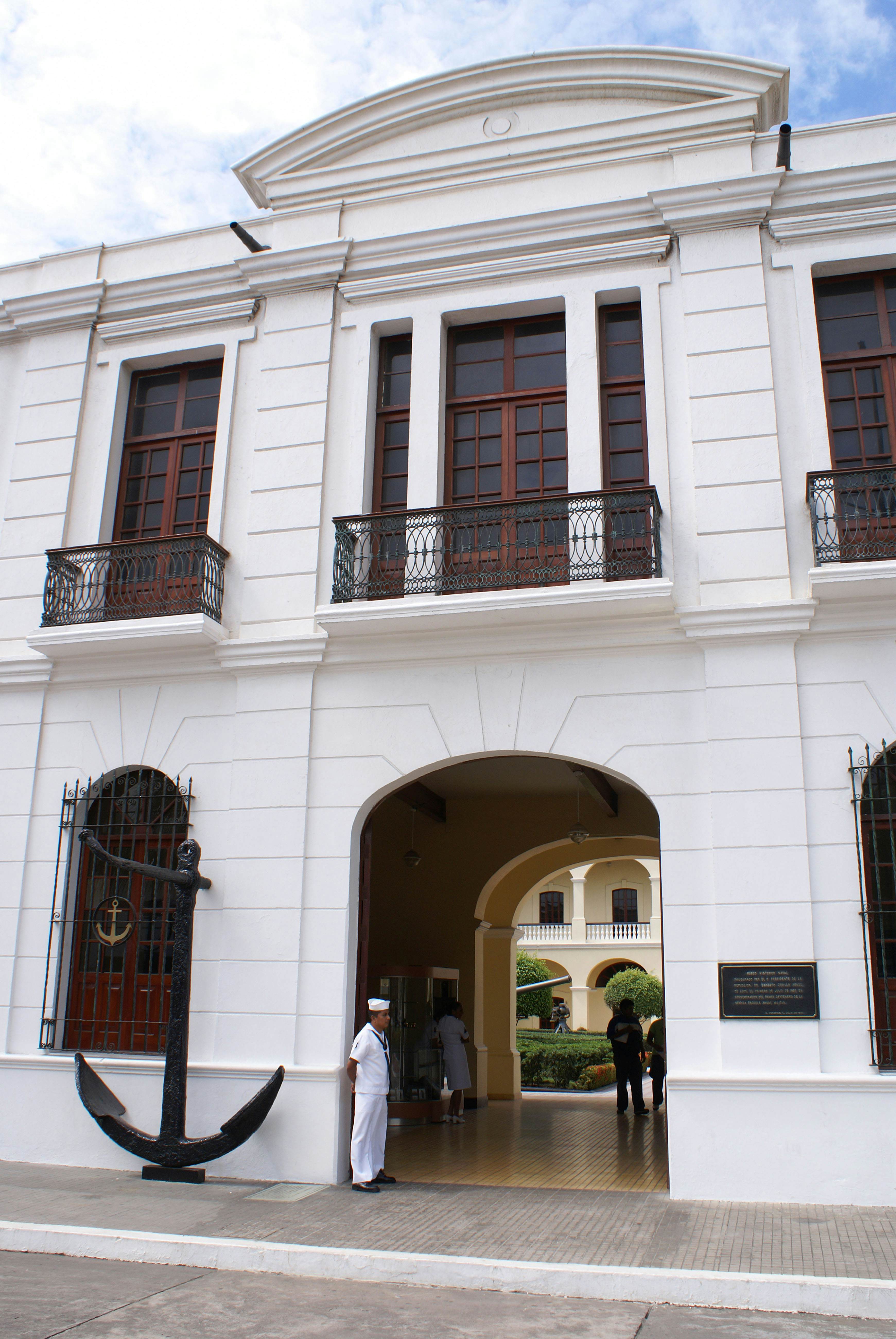 A Mexican sailor standing guard outside a naval museum entrance on a sunny day.