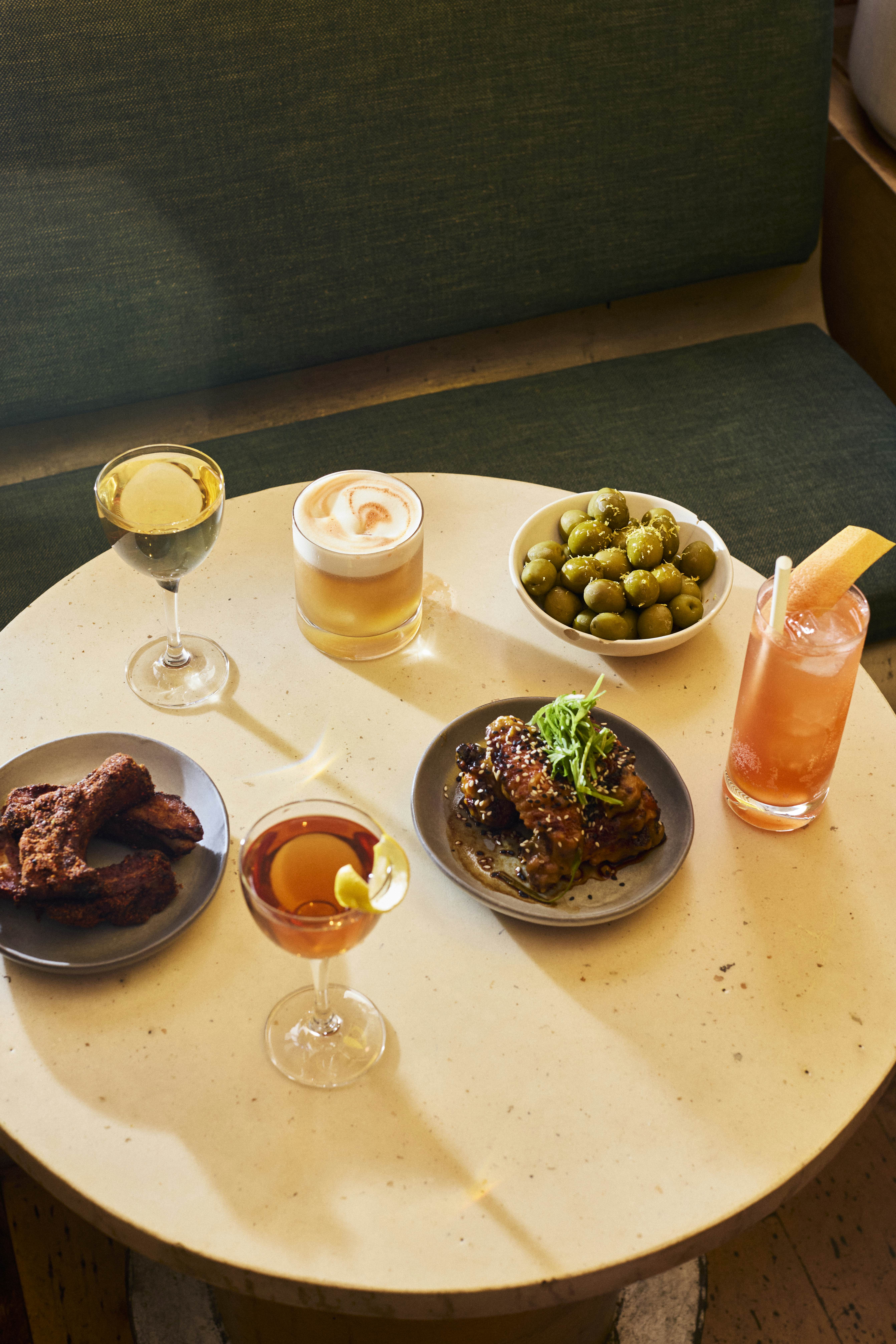 An overhead view of a white table with drinks and small plates of food.