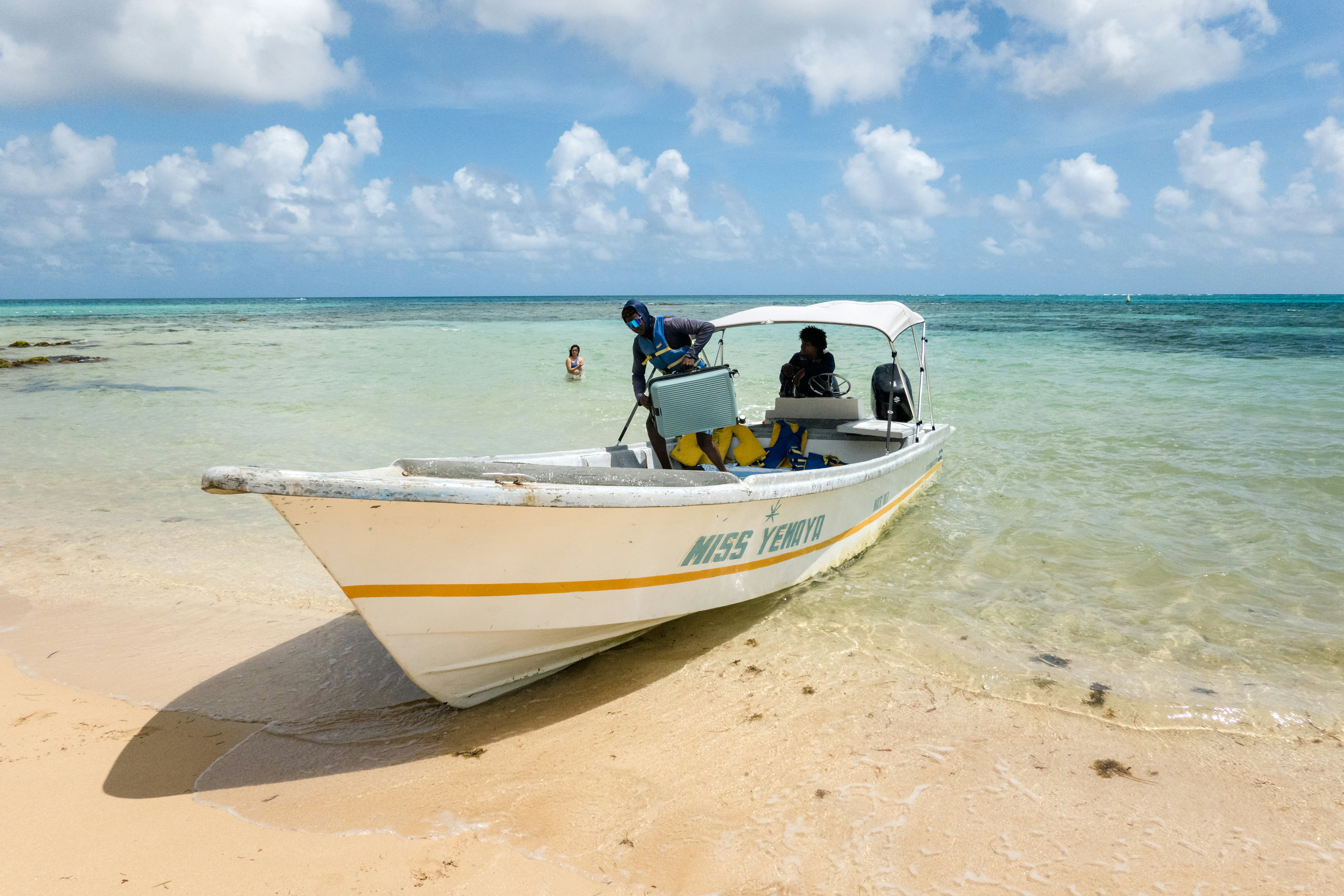 A small boat docks on a sandy beach. A person lifts a suitcase as they prepare to disembark.