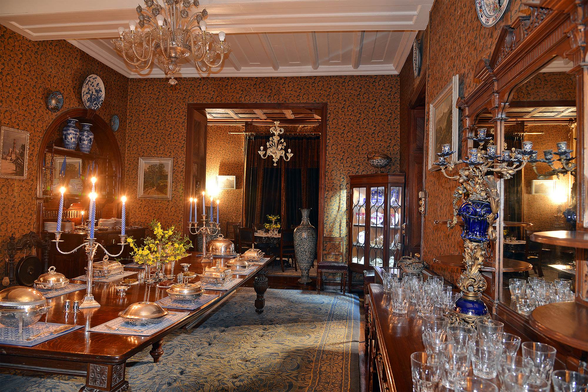 A large grand dining room with candles, ornate glasses and chandeliers.