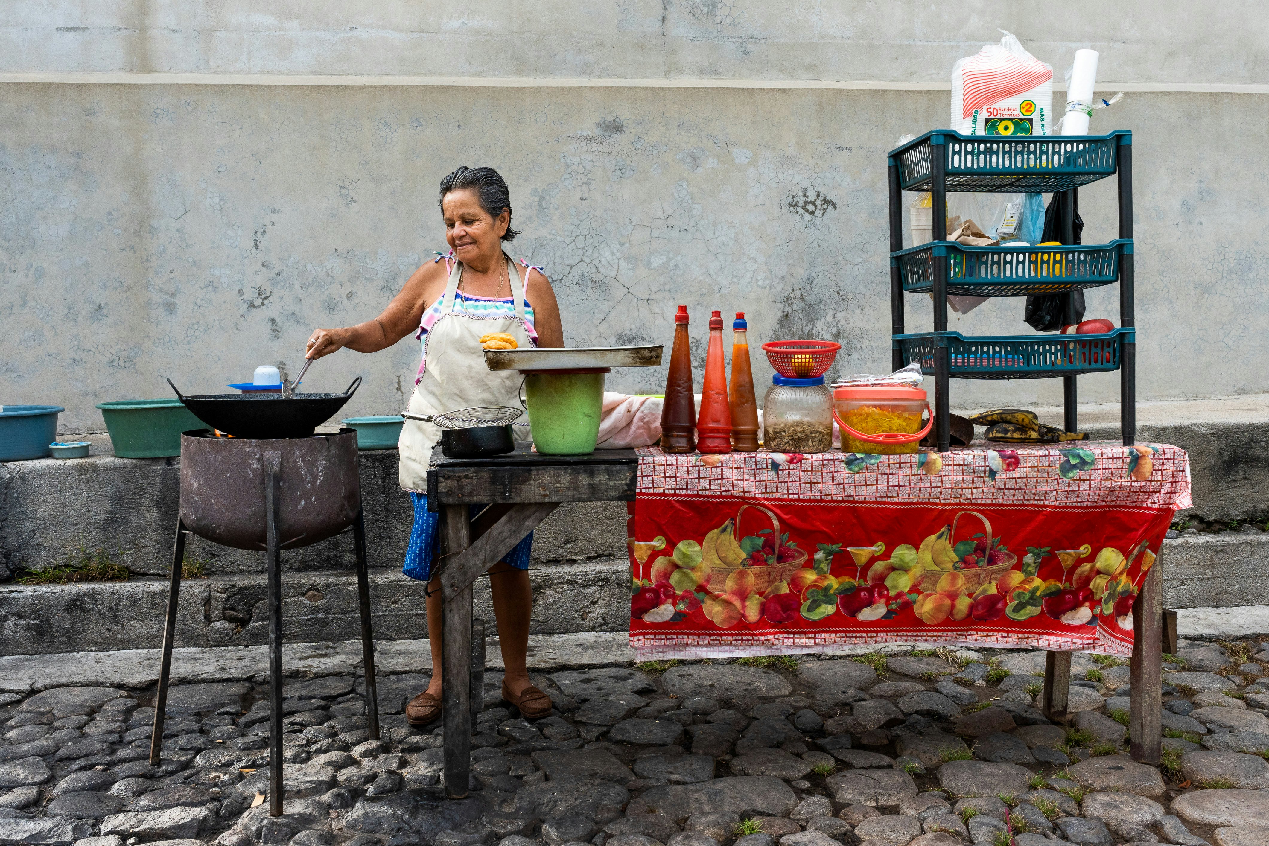 A female vendor in an apron cooking food at a streetside table