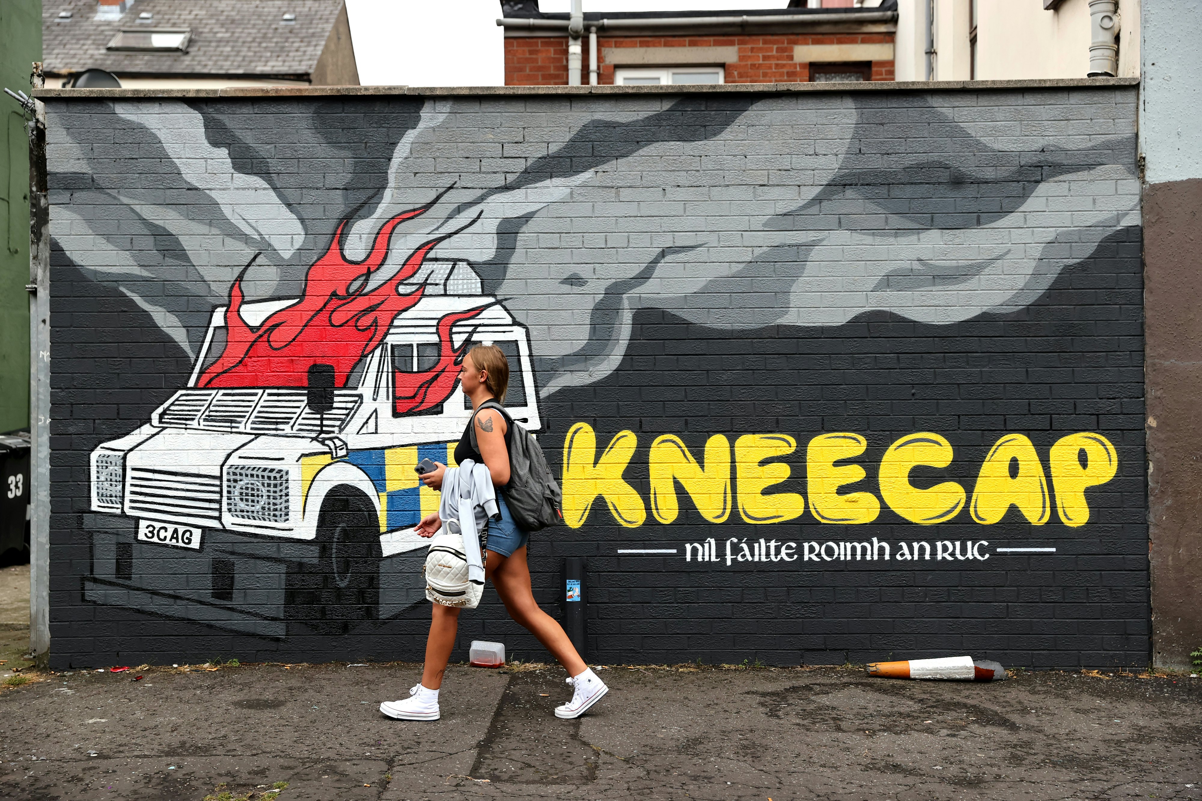 A person walks past a painted wall mural depicting a police car on fire.