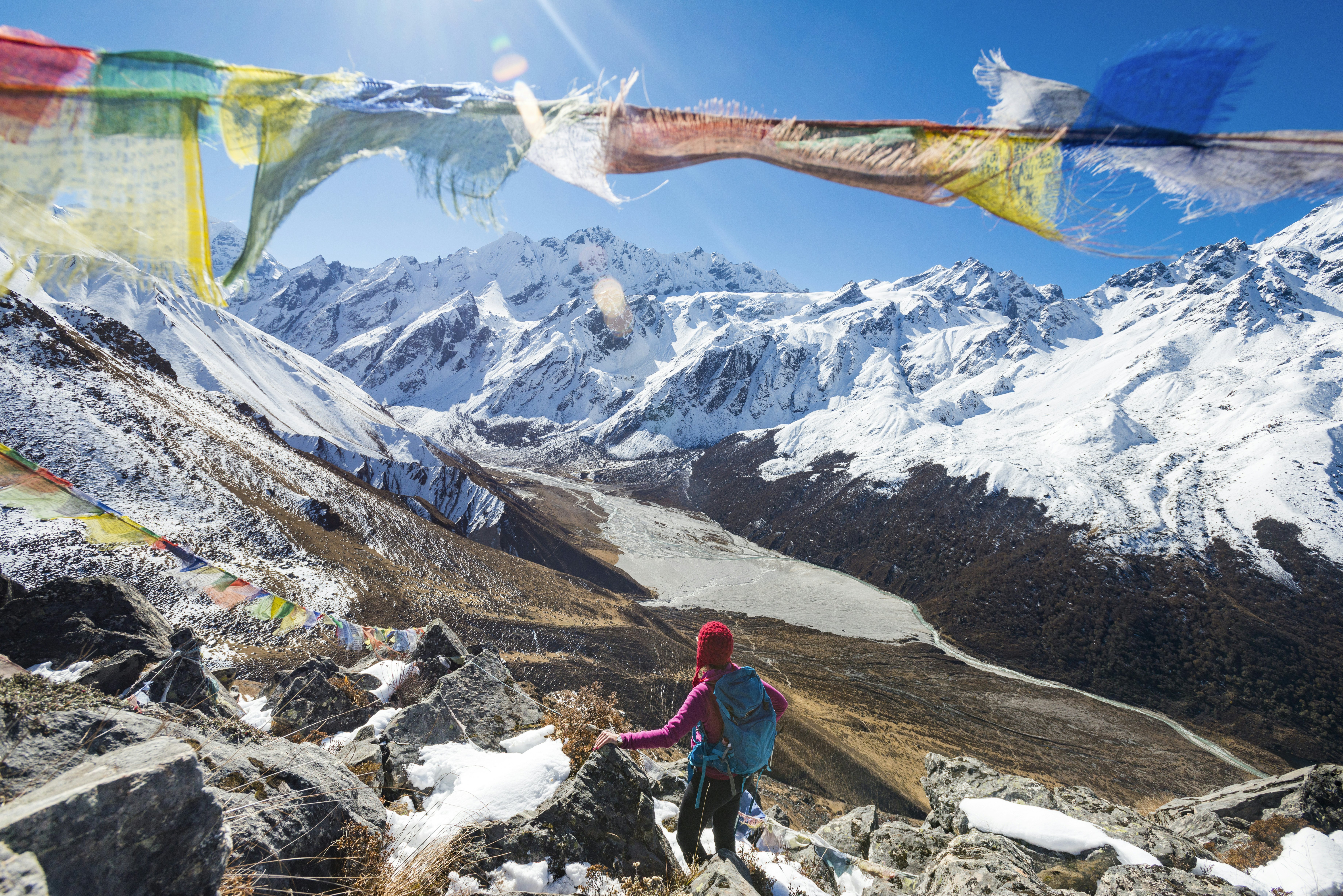 A woman trekking in the Langtang valley in Nepal stands on the top of Kyanjin Ri among prayer flags and looks out towards Ganchempo in the distance