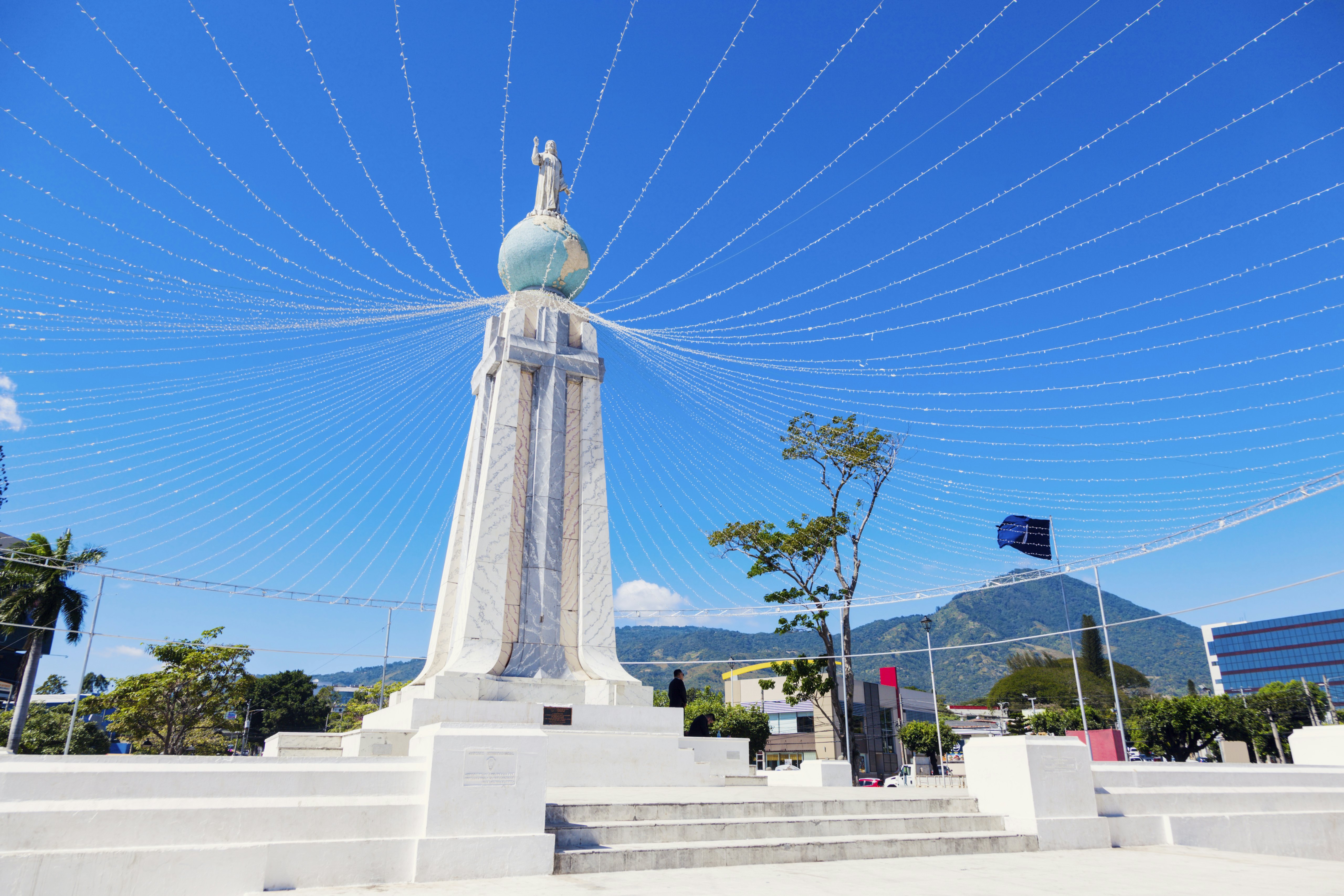 A large stone monument with a cross is topped by a globe with a figure standing on top.