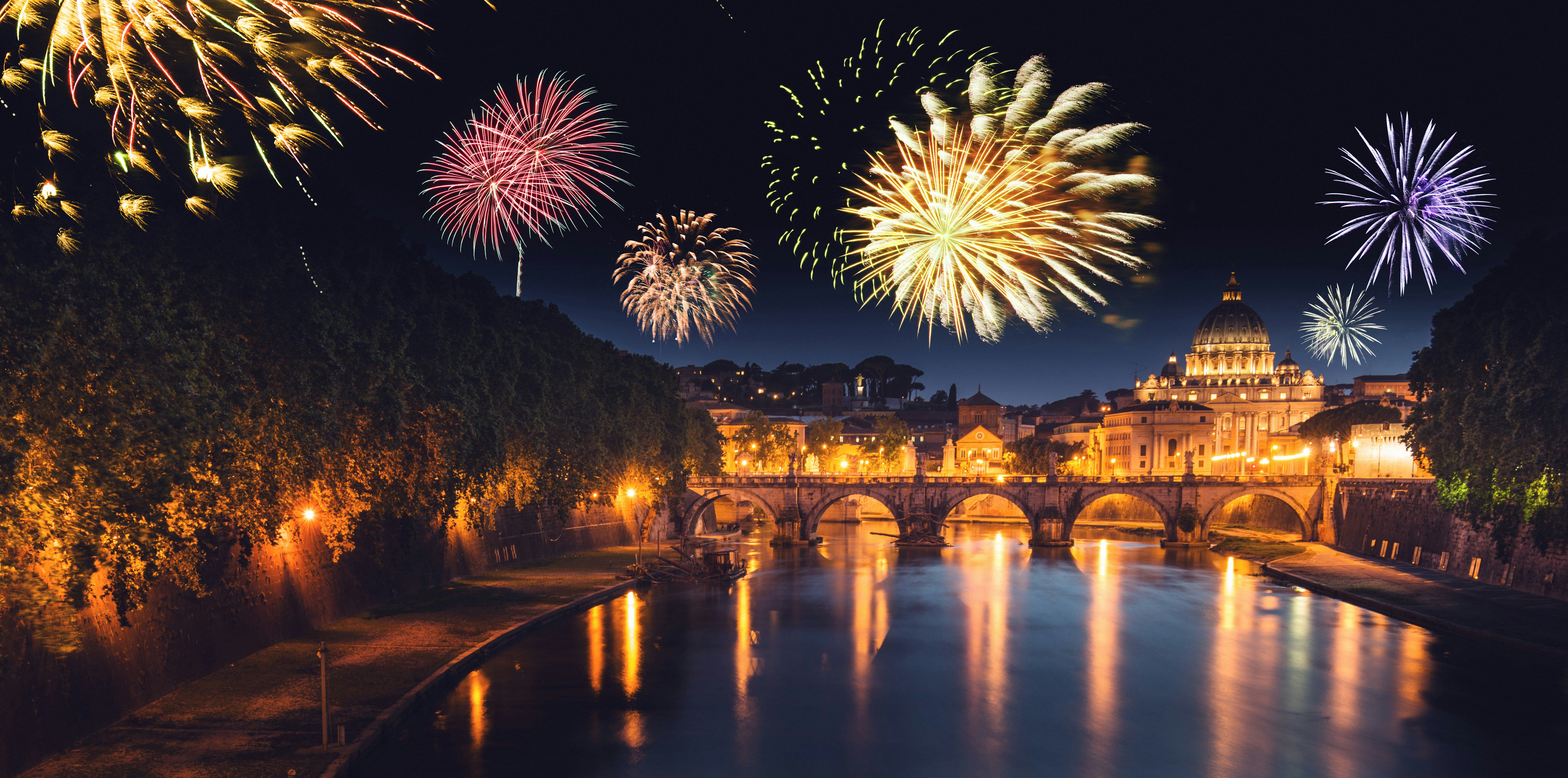 Colorful fireworks burst above a bridge and buildings along water