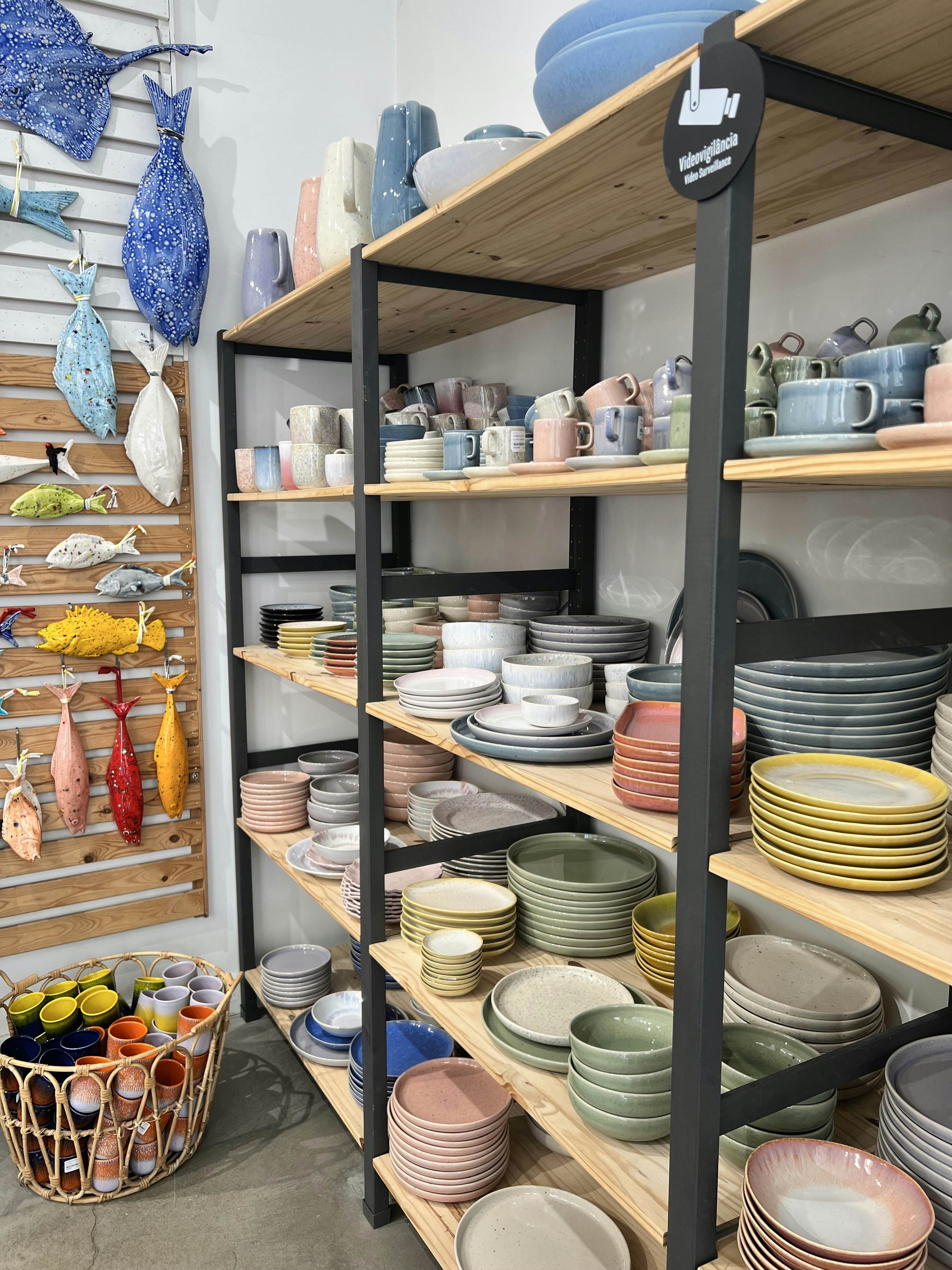 Colorful pottery plates and bowls are stacked on shelves, and ceramic fish are displayed on the wall.