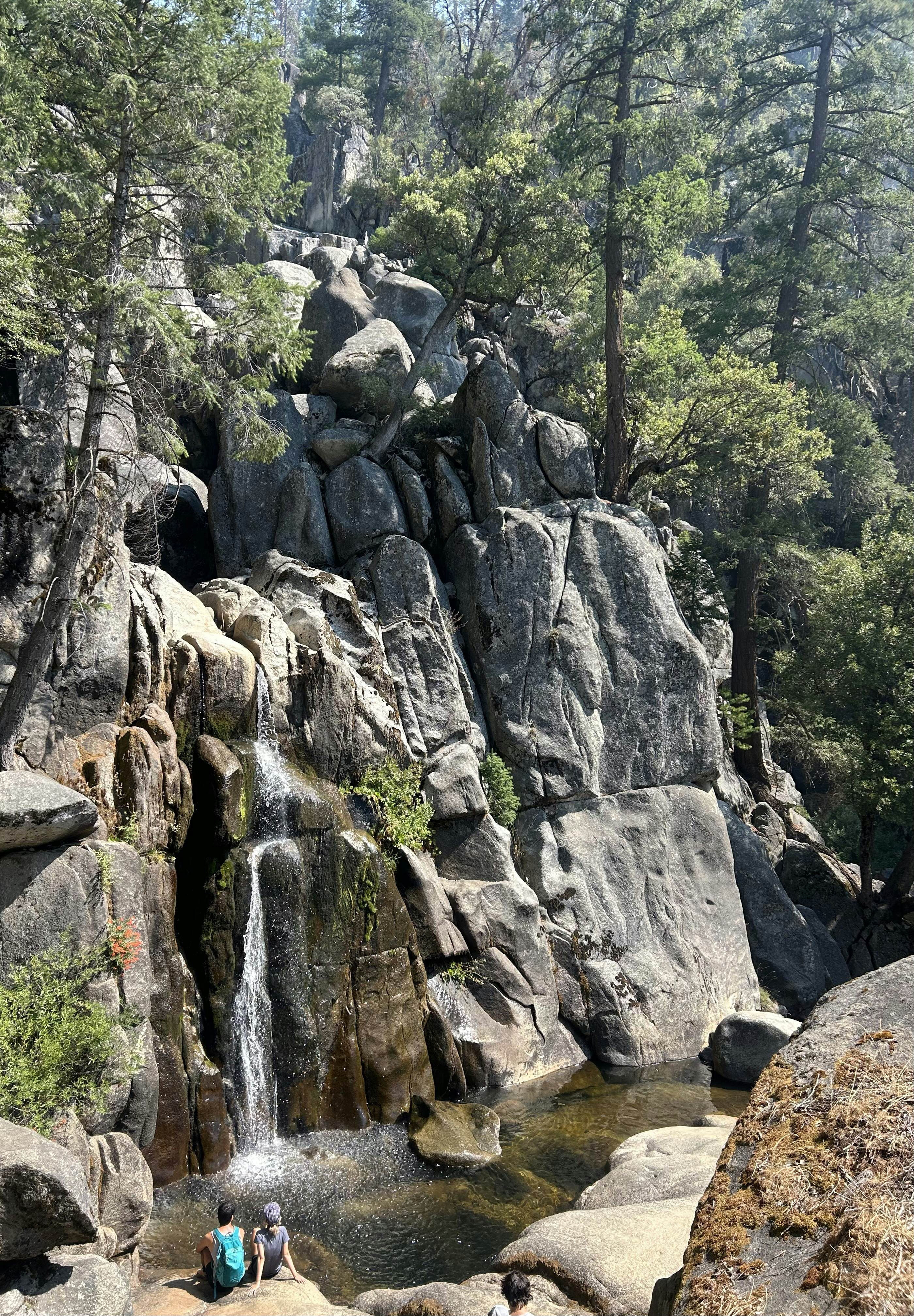 Two people sit on a rock near a waterfall in California.