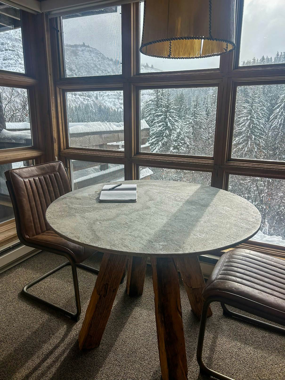 A journal and two chairs in front of a window with views of snowy trees.  