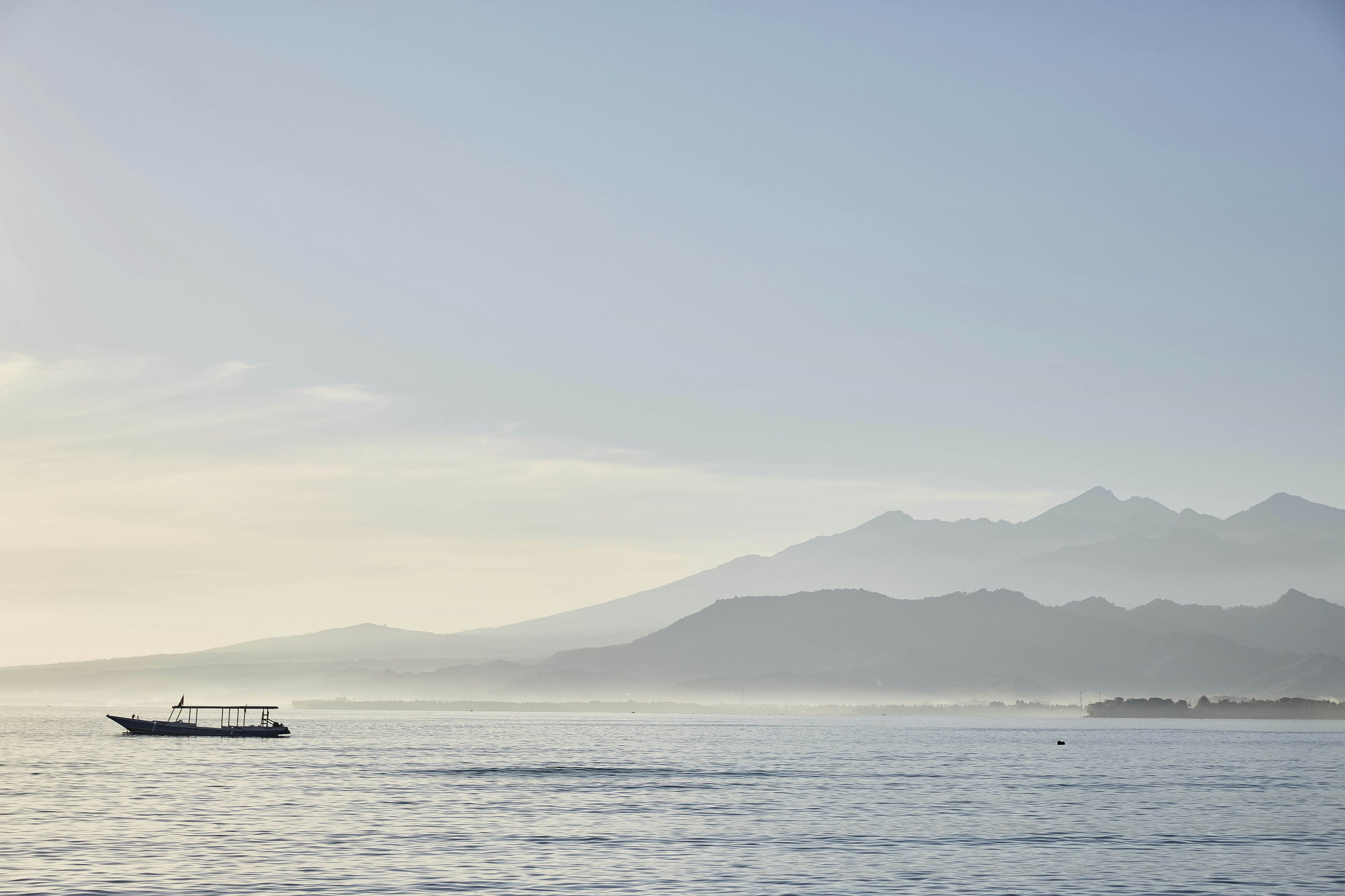 A boat moored in the sea with mountainous island in the distance on a hazy day.