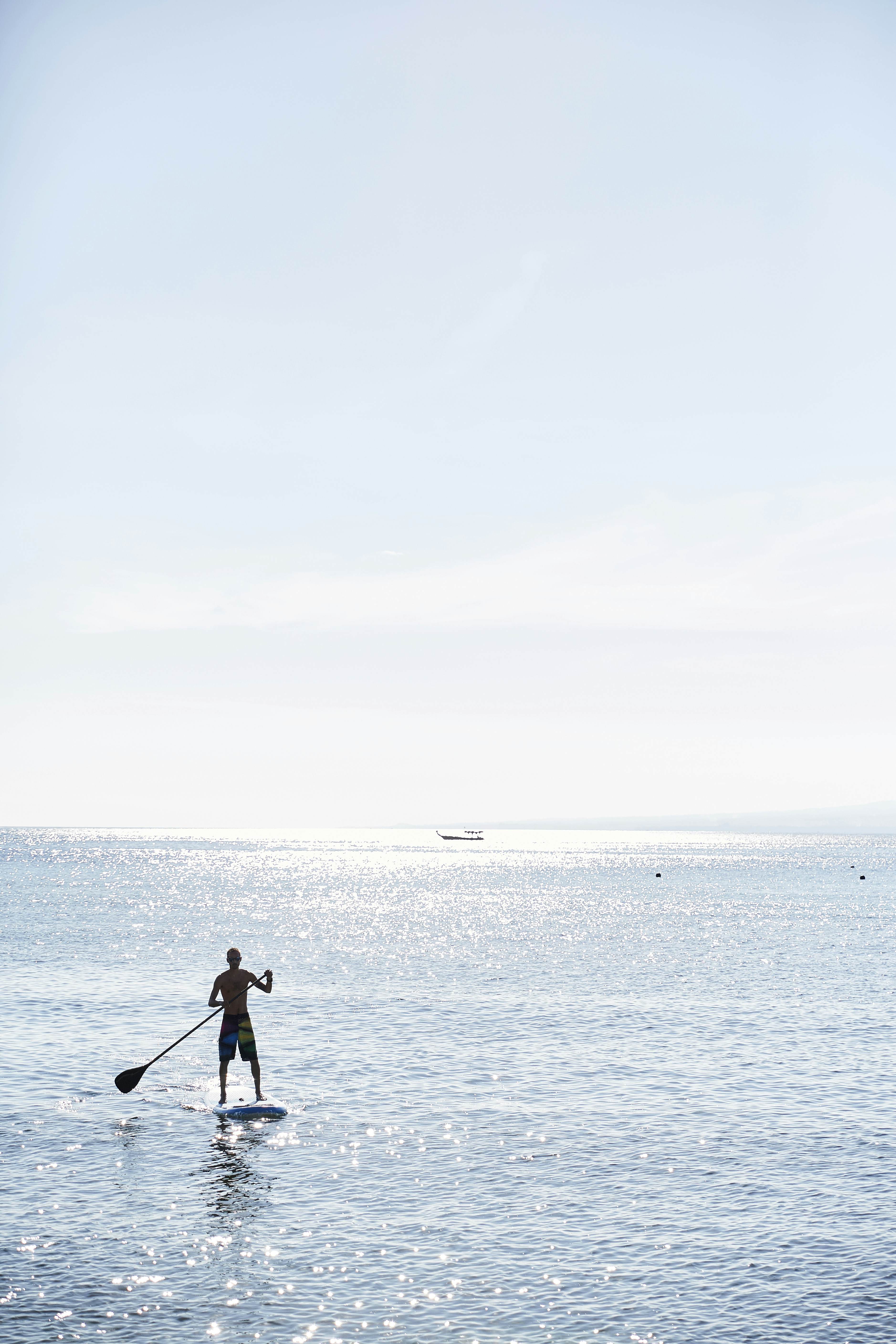 A silhouetted paddle boarder in the sea on a bright day.