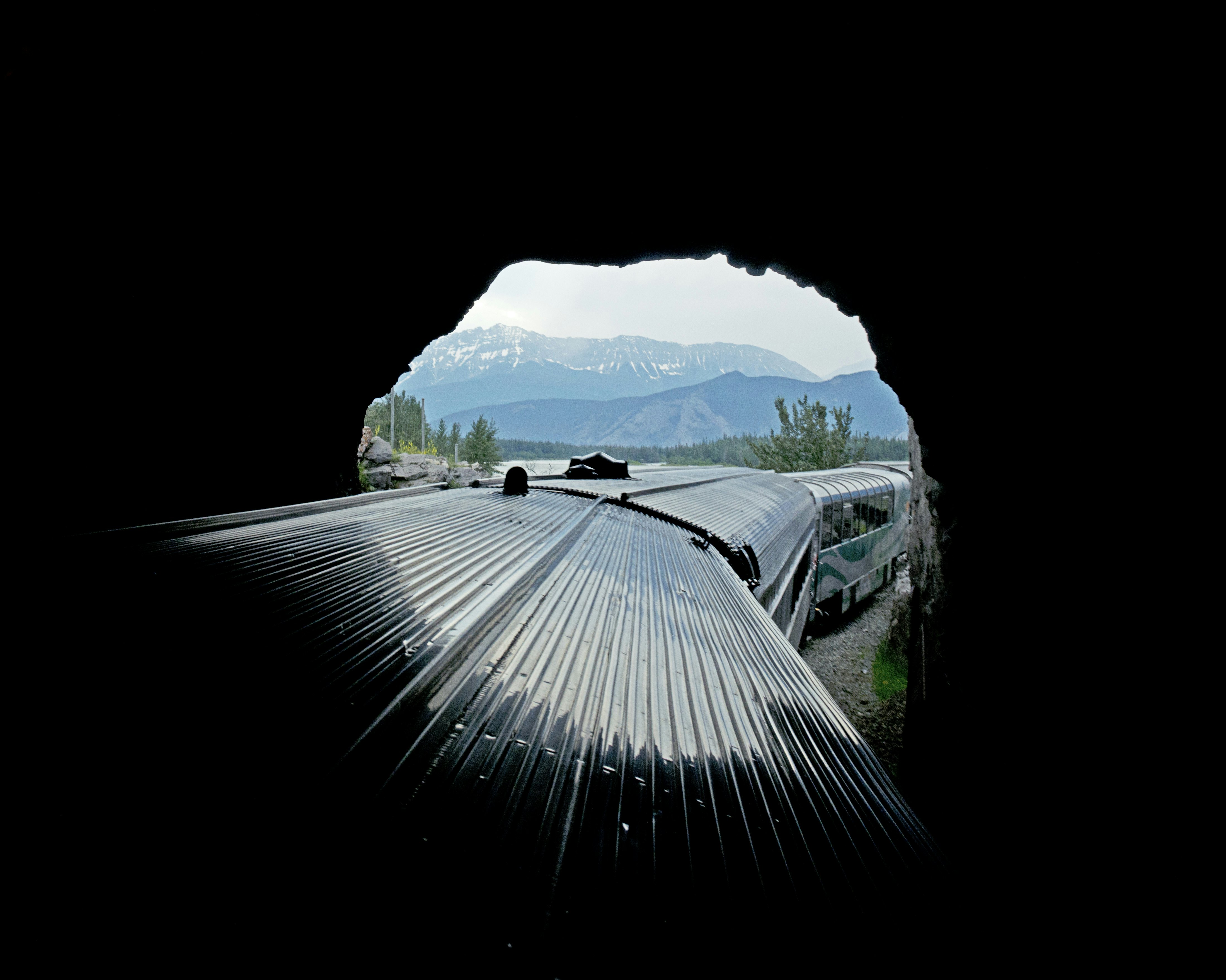 A train emerges from a dark tunnel into a mountainous landscape.