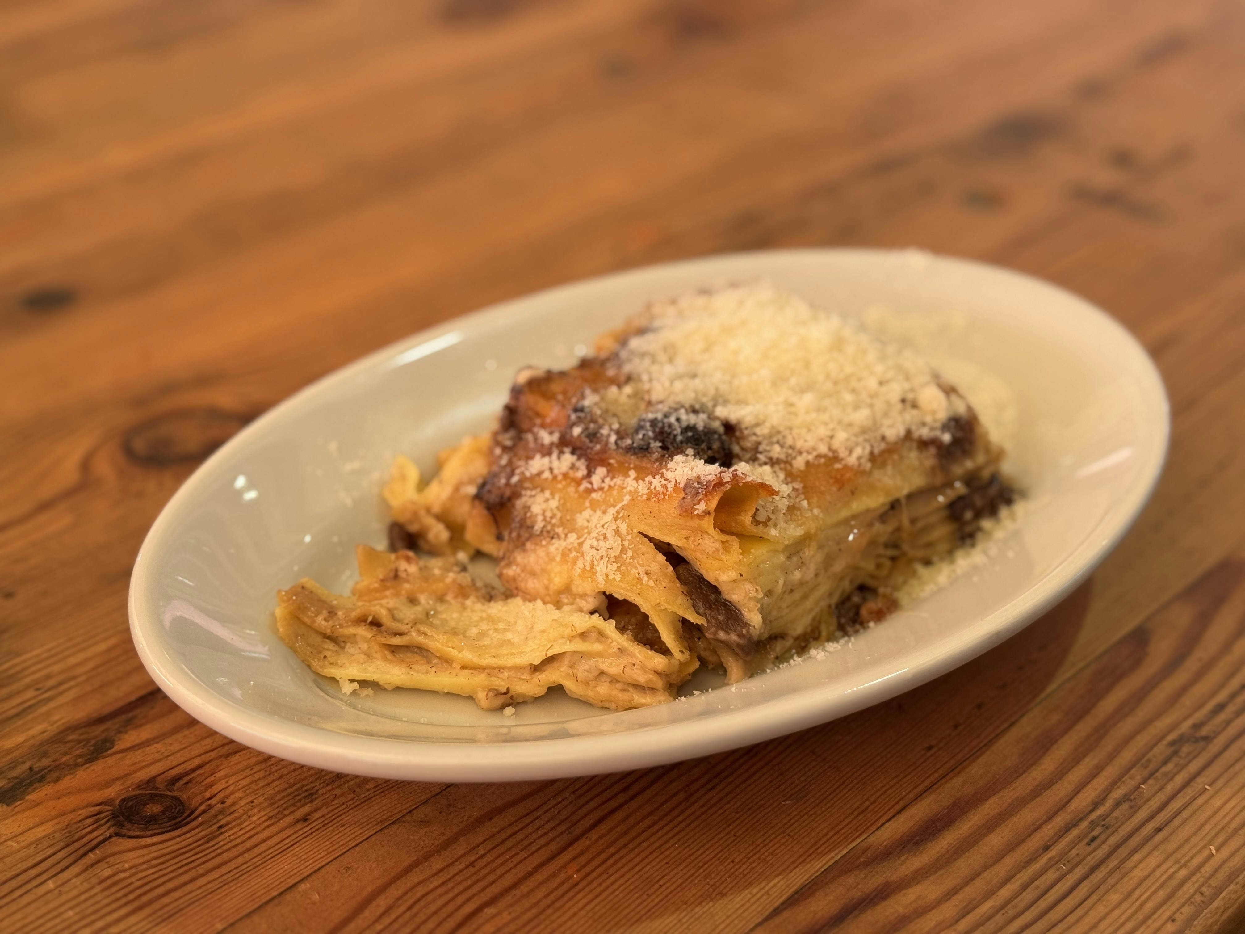 White plate with lasagna covered in parmesan cheese on a wooden table