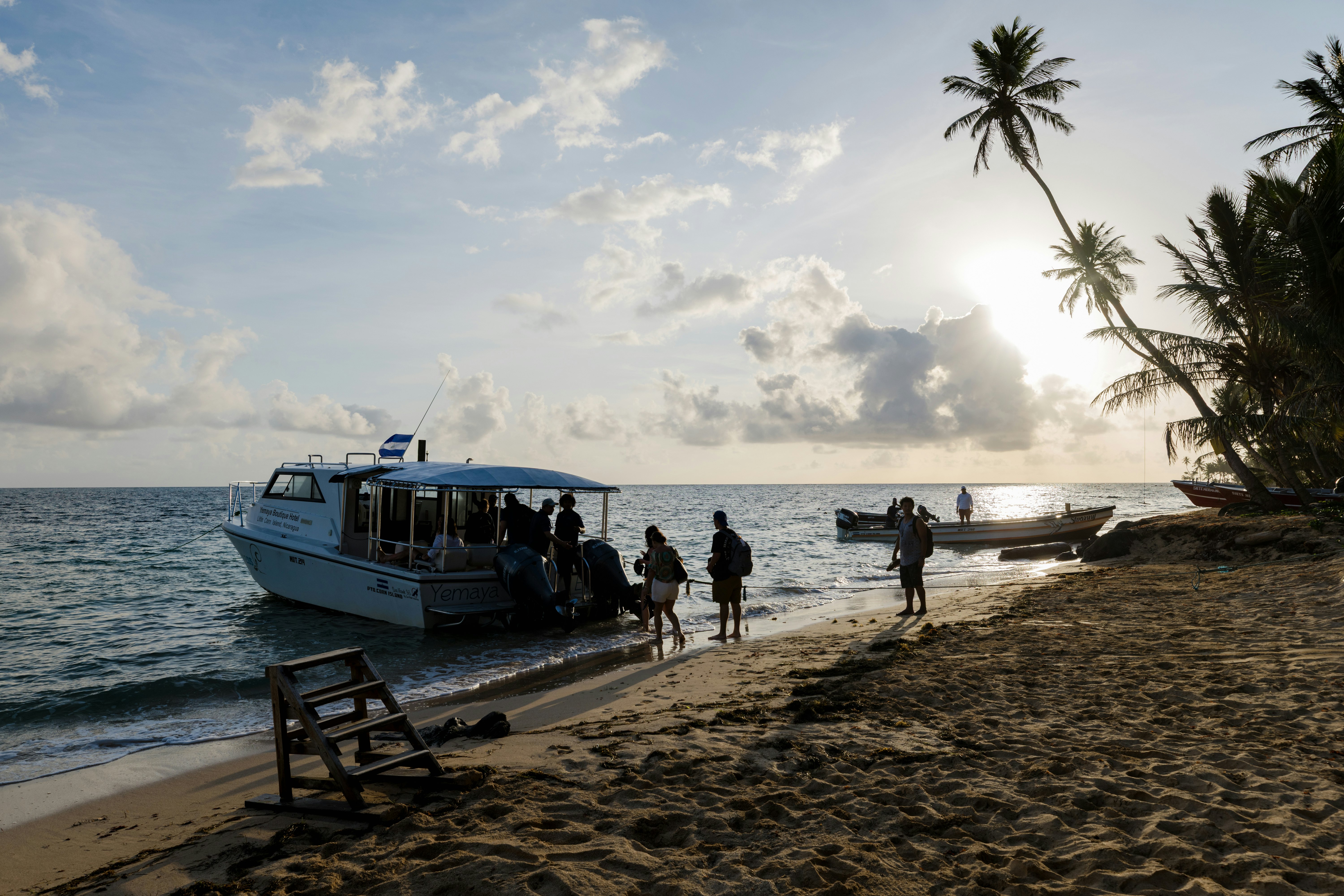People boarding a small boat directly from a sandy palm tree-lined beach.
