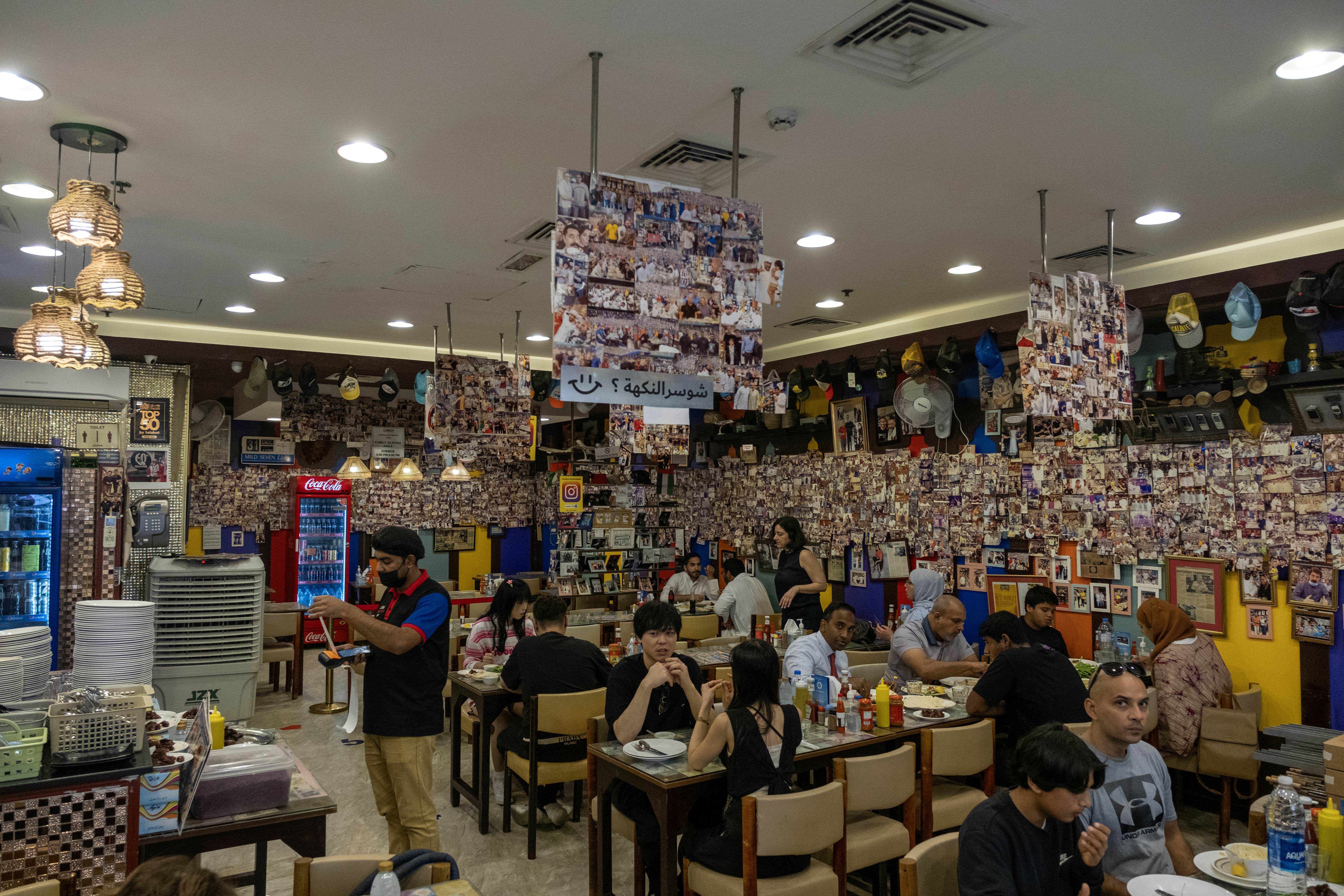 Busy interior of a kebab restaurant. Tables are full of customers and the walls are covered in photographs