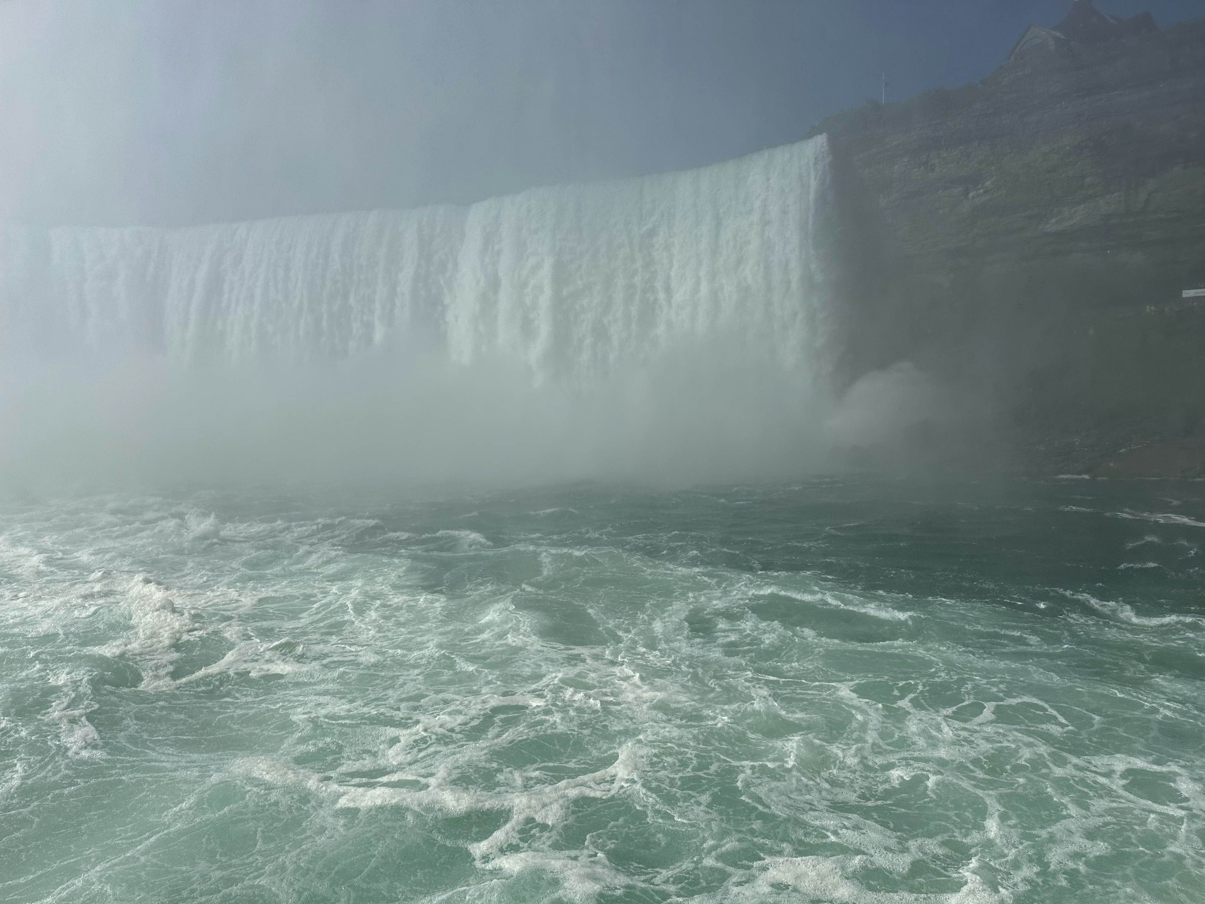 Falls from above with Rainbow arching over red Maid of the Mist boat. 