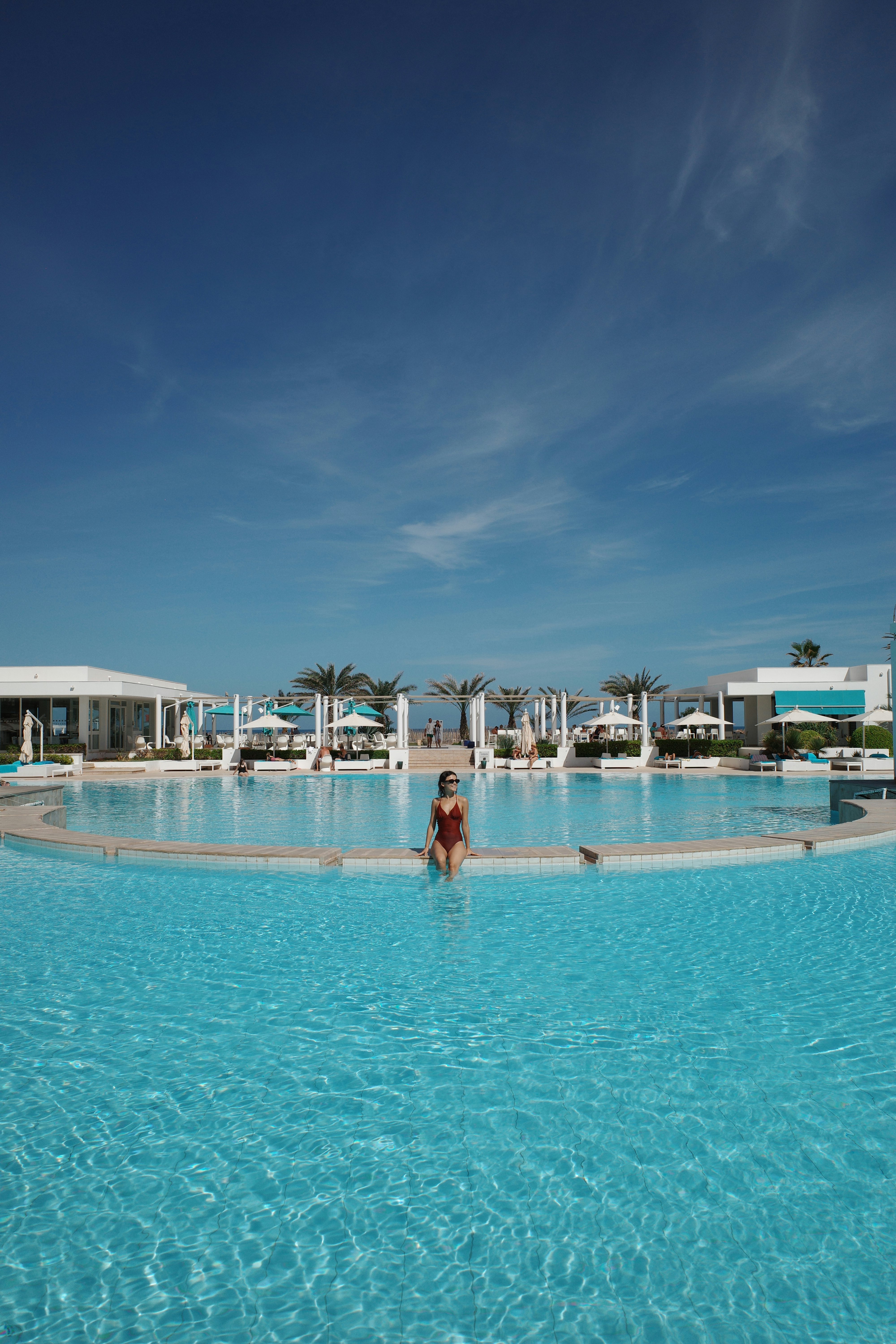 A woman in a large pool with palm trees in the background