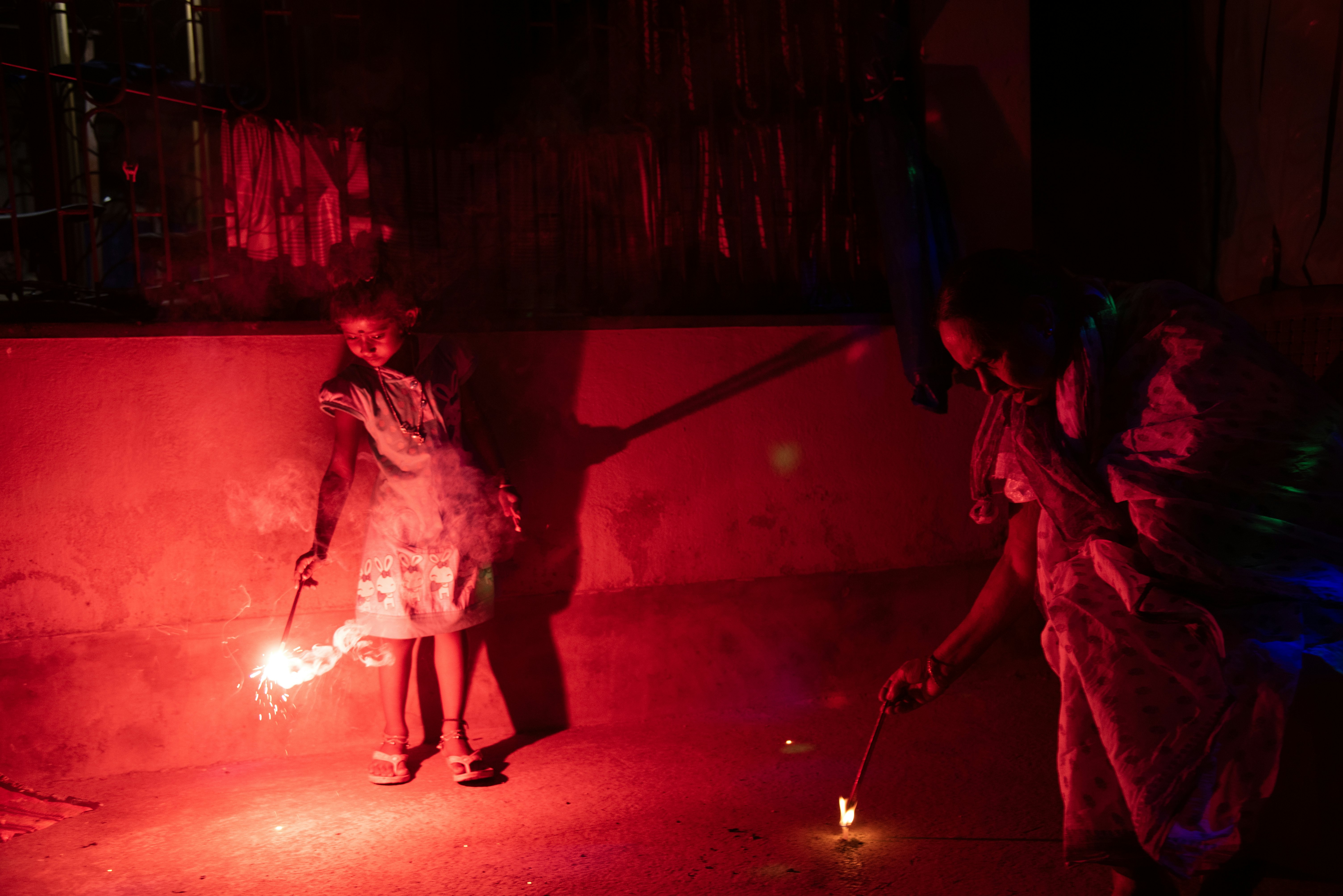 A child and her grandmother lighting firecrackers at night