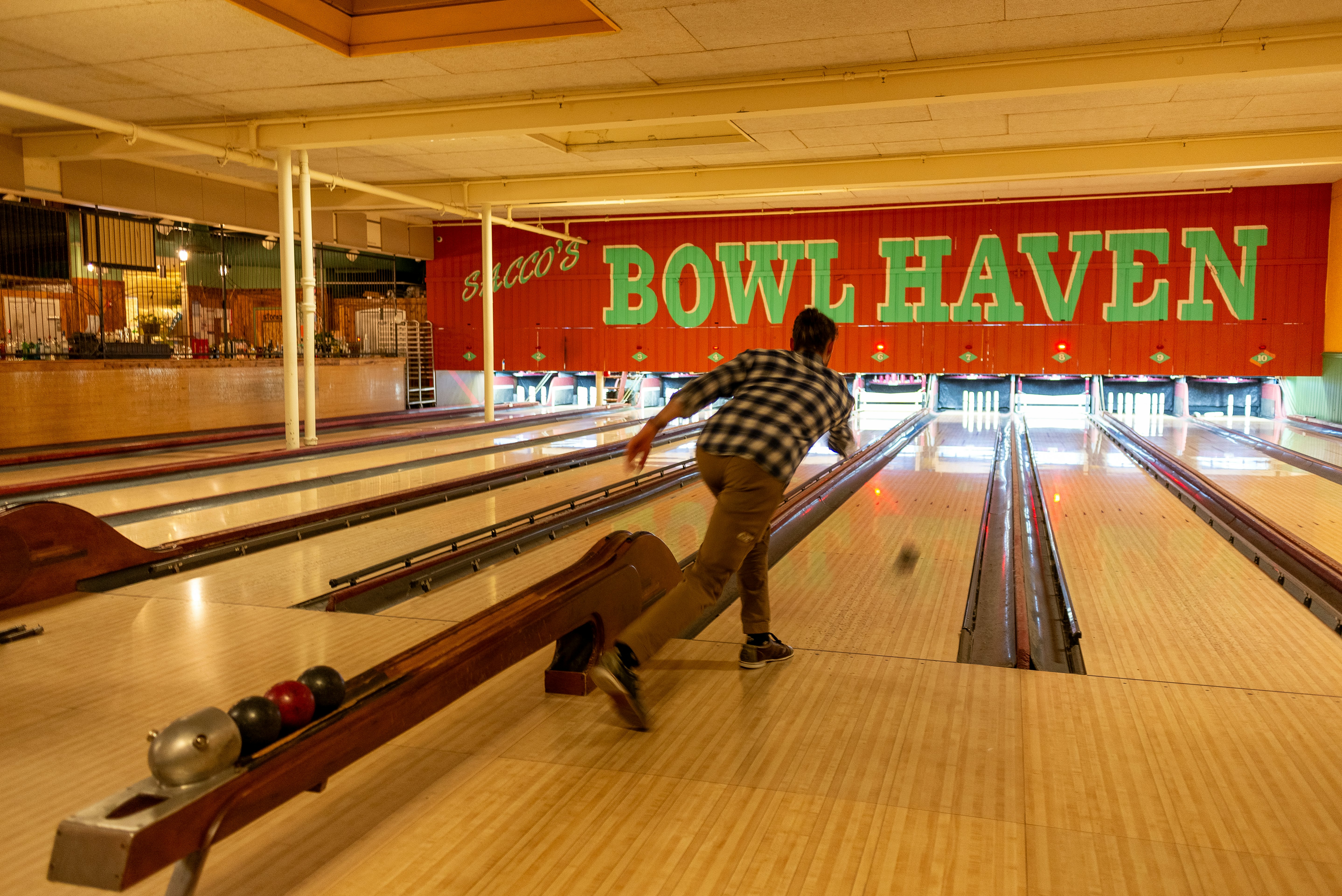 Person bowling with small ball going down a lane toward candlepins