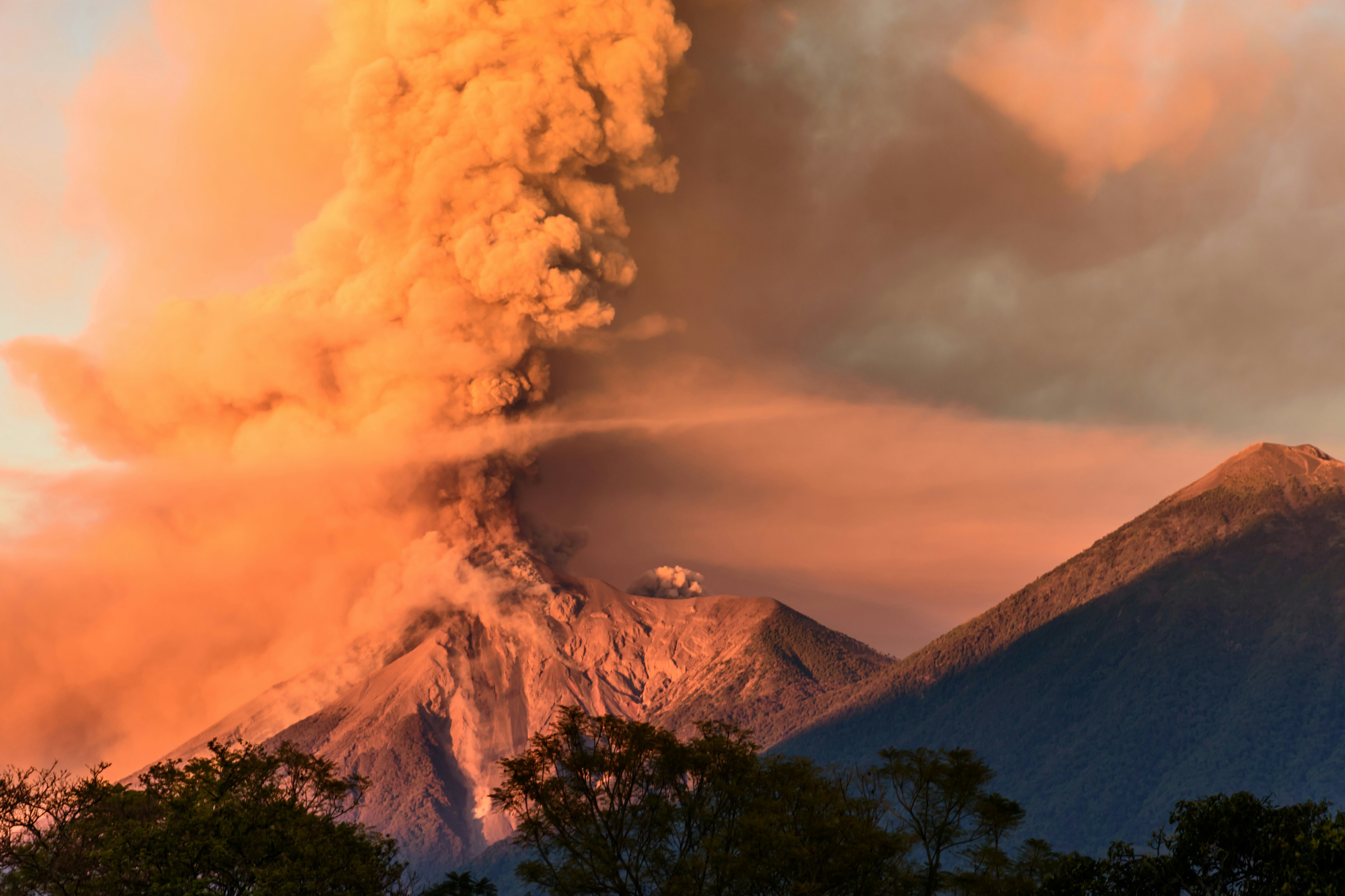 A volcano erupting at dawn next to a dormant volcano.