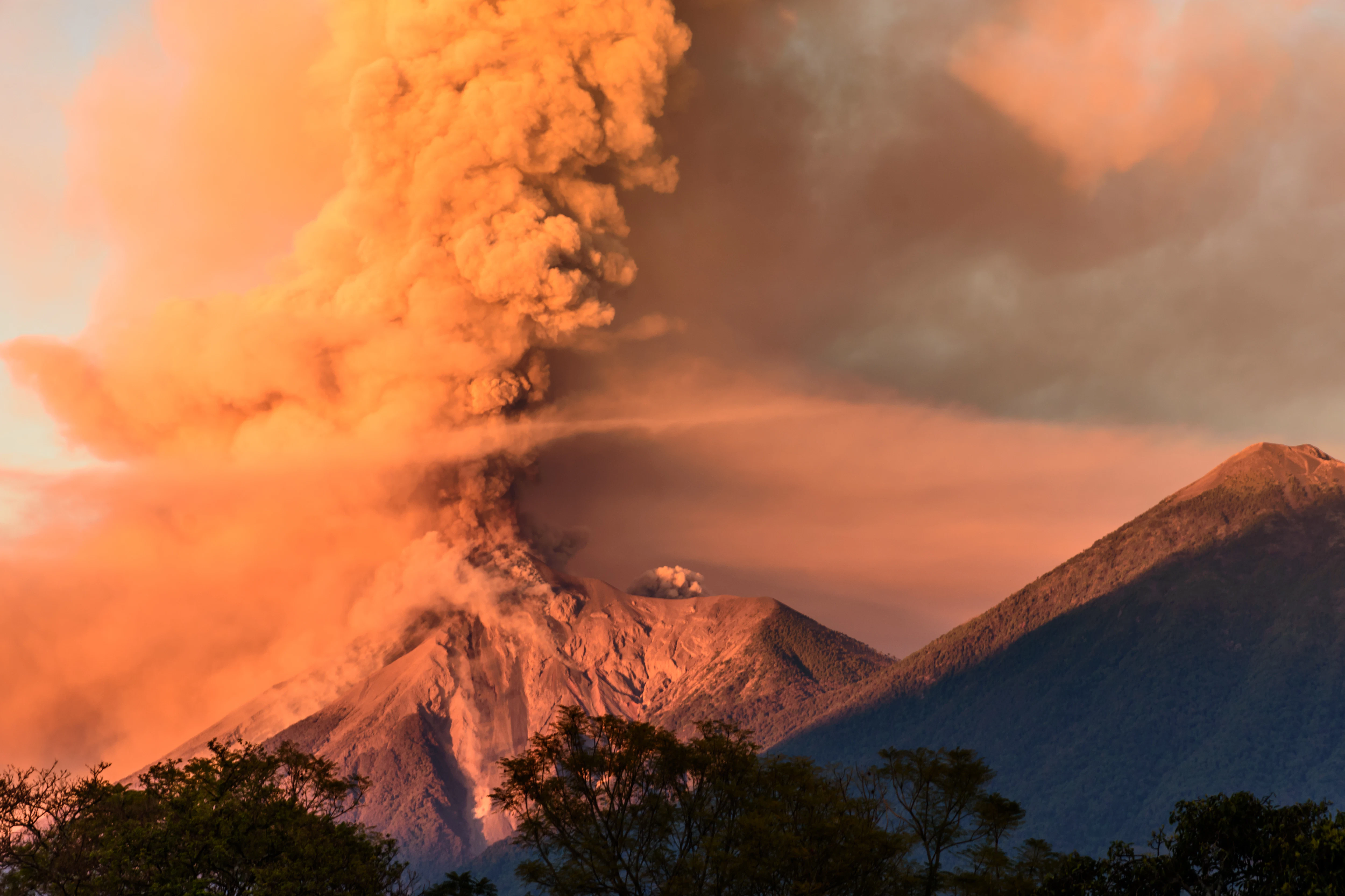 A volcano erupting at dawn next to a dormant volcano.