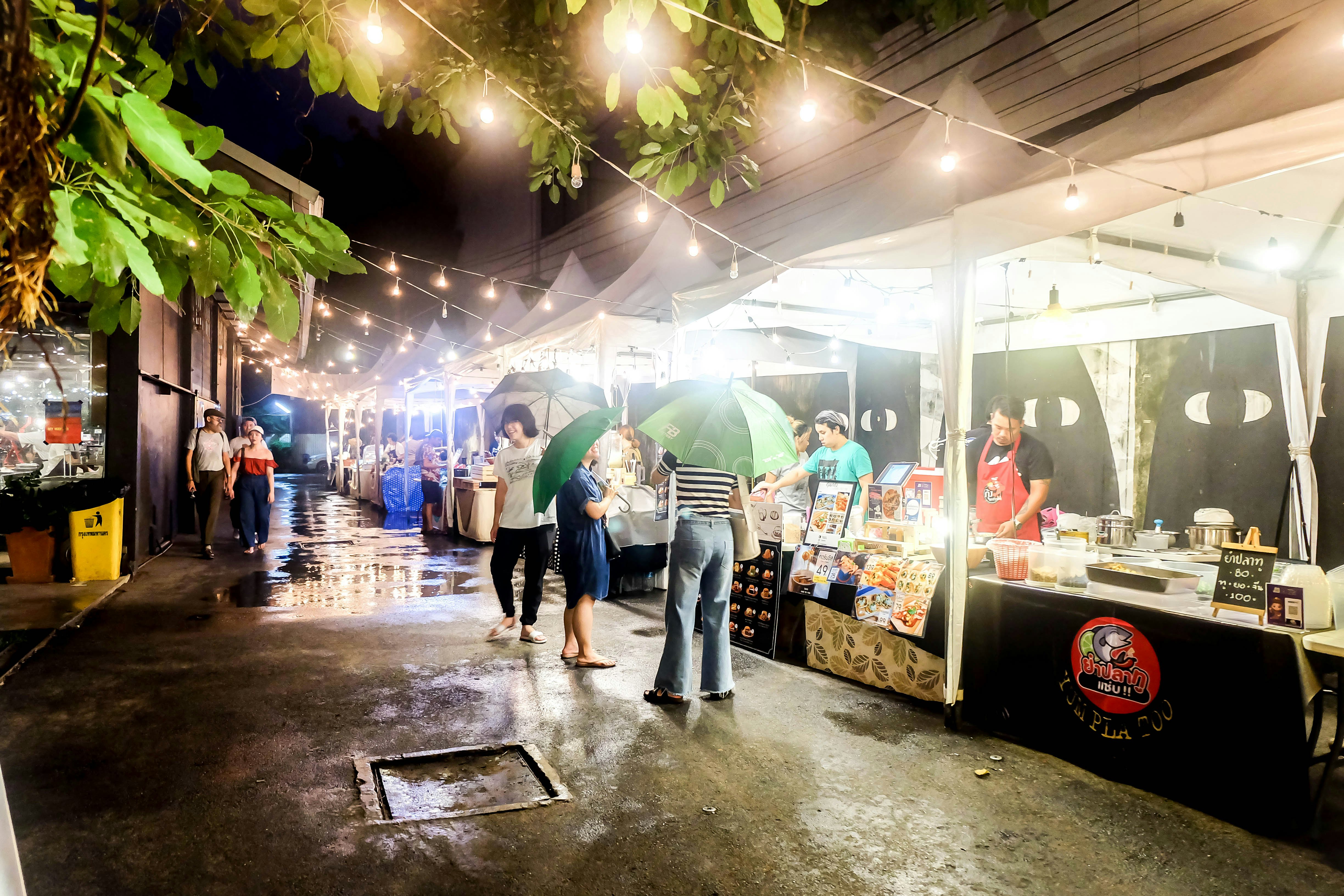 A group of people with umbrellas in front of food sellers.
