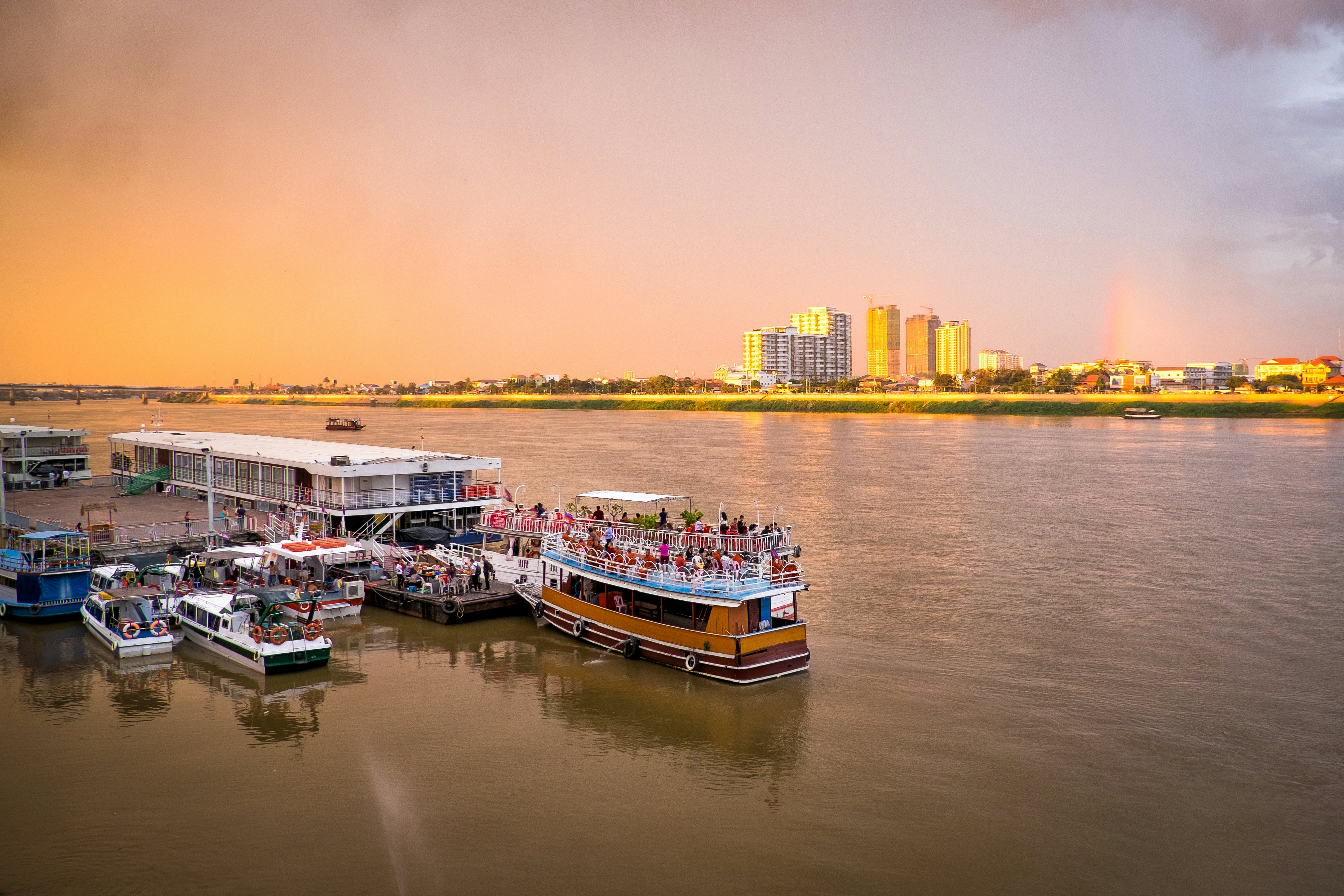 Tourist boats on a pier with a city skyline on the opposite side of the river